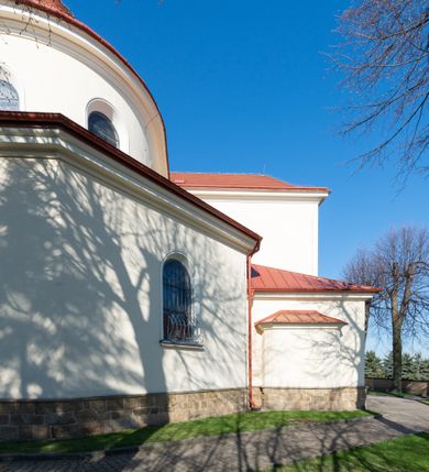 Zdjęcie nr 18: Kościół murowany, orientowany, jednonawowy, z transeptem, prezbiterium z obejściem i przybudówkami. Od zachodu kruchta, od północy kwadratowa kaplica, od południa kolejna przybudówka. 
Prezbiterium zamknięte półokrągło, z obejściem przeprutym do niego arkadami wspartymi na filarach. Ściany nawy i prezbiterium gładkie, przekryte sklepieniem kolebkowym z lunetami, w których mieszczą się okna. Transept i przecięcie naw sklepione krzyżowo. Na ścianach polichromia figuralna ze scenami z Nowego Testamentu, w partii sklepienia drobne, złote gwiazdki. Od zachodu chór zatopiony w występującym asymetrycznie murze, z tralkową balustradą. W prezbiterium siedem okien w kształcie stojącego prostokąta zamkniętego łukiem pełnym wypełnionych witrażami, w nawie sześć okien, w ramionach transeptu po jednym, czterodzielnym, wypełnionym witrażem, na wysokości chóru po dwa z każdej strony. Główne wejście od zachodu przez kruchtę. Fasada poprzedzona przedsionkiem o podziałach ramowych, z prostokątnym wejściem na osi, flankowanym parą pilastrów i prostokątnymi płycinami. Kondygnację wieńczy pełne belkowanie z wysuniętym gzymsem podtrzymującym daszek i trójkątny, schodkowy szczyt zakończony postumentami. Na centralnym krzyż, na sąsiadujących figury dzieci z rogami obfitości, a na zewnętrznych wazony płomieniste; szczyt ujmują postumenty z kulami. Fasada dwukondygnacyjna ze szczytem. Kondygnacja trójosiowa, rozdzielona pilastrami, o polach wypełnionych blendami w kształcie stojących prostokątów zamkniętych łukiem pełnym; szczyt trójkątny, z tarczą zegarową pośrodku. Budynek kościoła o wyraźnych podziałach na bryły składowe, ściany gładkie, przeprute oknami, z gzymsami pod krawędziami dachu. 
Nad nawą główną, na kalenicy, wieżyczka na sygnaturkę z latarnią i baniastym hełmem, druga na skrzyżowaniu naw, z latarnią i  hełmem zakończonym krzyżem. Dach nad nawą główną i przedsionkiem dwuspadowy, nad ramionami transeptu trójspadowym,nad prezbiterium zakończony wielobocznie, na przybudówkach dachy pulpitowe, dwuspadowe i wielospadowe. Dachy kryte dachówką ceramiczną, wieżyczki blachą. 
Najciekawszymi zabytkami kościoła są ołtarz główny z około 1700 roku z nastawą utworzoną z wici winnej latorośli, manierystyczny ołtarz boczny oraz siedemnastowieczna chrzcielnica z warsztatu Santi Gucciego. 
