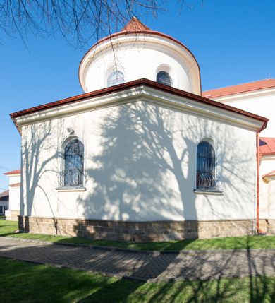 Zdjęcie nr 20: Kościół murowany, orientowany, jednonawowy, z transeptem, prezbiterium z obejściem i przybudówkami. Od zachodu kruchta, od północy kwadratowa kaplica, od południa kolejna przybudówka. 
Prezbiterium zamknięte półokrągło, z obejściem przeprutym do niego arkadami wspartymi na filarach. Ściany nawy i prezbiterium gładkie, przekryte sklepieniem kolebkowym z lunetami, w których mieszczą się okna. Transept i przecięcie naw sklepione krzyżowo. Na ścianach polichromia figuralna ze scenami z Nowego Testamentu, w partii sklepienia drobne, złote gwiazdki. Od zachodu chór zatopiony w występującym asymetrycznie murze, z tralkową balustradą. W prezbiterium siedem okien w kształcie stojącego prostokąta zamkniętego łukiem pełnym wypełnionych witrażami, w nawie sześć okien, w ramionach transeptu po jednym, czterodzielnym, wypełnionym witrażem, na wysokości chóru po dwa z każdej strony. Główne wejście od zachodu przez kruchtę. Fasada poprzedzona przedsionkiem o podziałach ramowych, z prostokątnym wejściem na osi, flankowanym parą pilastrów i prostokątnymi płycinami. Kondygnację wieńczy pełne belkowanie z wysuniętym gzymsem podtrzymującym daszek i trójkątny, schodkowy szczyt zakończony postumentami. Na centralnym krzyż, na sąsiadujących figury dzieci z rogami obfitości, a na zewnętrznych wazony płomieniste; szczyt ujmują postumenty z kulami. Fasada dwukondygnacyjna ze szczytem. Kondygnacja trójosiowa, rozdzielona pilastrami, o polach wypełnionych blendami w kształcie stojących prostokątów zamkniętych łukiem pełnym; szczyt trójkątny, z tarczą zegarową pośrodku. Budynek kościoła o wyraźnych podziałach na bryły składowe, ściany gładkie, przeprute oknami, z gzymsami pod krawędziami dachu. 
Nad nawą główną, na kalenicy, wieżyczka na sygnaturkę z latarnią i baniastym hełmem, druga na skrzyżowaniu naw, z latarnią i  hełmem zakończonym krzyżem. Dach nad nawą główną i przedsionkiem dwuspadowy, nad ramionami transeptu trójspadowym,nad prezbiterium zakończony wielobocznie, na przybudówkach dachy pulpitowe, dwuspadowe i wielospadowe. Dachy kryte dachówką ceramiczną, wieżyczki blachą. 
Najciekawszymi zabytkami kościoła są ołtarz główny z około 1700 roku z nastawą utworzoną z wici winnej latorośli, manierystyczny ołtarz boczny oraz siedemnastowieczna chrzcielnica z warsztatu Santi Gucciego. 
