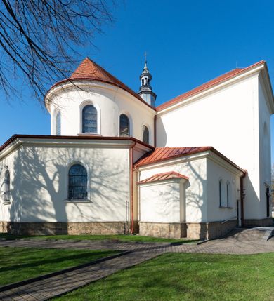 Zdjęcie nr 21: Kościół murowany, orientowany, jednonawowy, z transeptem, prezbiterium z obejściem i przybudówkami. Od zachodu kruchta, od północy kwadratowa kaplica, od południa kolejna przybudówka. 
Prezbiterium zamknięte półokrągło, z obejściem przeprutym do niego arkadami wspartymi na filarach. Ściany nawy i prezbiterium gładkie, przekryte sklepieniem kolebkowym z lunetami, w których mieszczą się okna. Transept i przecięcie naw sklepione krzyżowo. Na ścianach polichromia figuralna ze scenami z Nowego Testamentu, w partii sklepienia drobne, złote gwiazdki. Od zachodu chór zatopiony w występującym asymetrycznie murze, z tralkową balustradą. W prezbiterium siedem okien w kształcie stojącego prostokąta zamkniętego łukiem pełnym wypełnionych witrażami, w nawie sześć okien, w ramionach transeptu po jednym, czterodzielnym, wypełnionym witrażem, na wysokości chóru po dwa z każdej strony. Główne wejście od zachodu przez kruchtę. Fasada poprzedzona przedsionkiem o podziałach ramowych, z prostokątnym wejściem na osi, flankowanym parą pilastrów i prostokątnymi płycinami. Kondygnację wieńczy pełne belkowanie z wysuniętym gzymsem podtrzymującym daszek i trójkątny, schodkowy szczyt zakończony postumentami. Na centralnym krzyż, na sąsiadujących figury dzieci z rogami obfitości, a na zewnętrznych wazony płomieniste; szczyt ujmują postumenty z kulami. Fasada dwukondygnacyjna ze szczytem. Kondygnacja trójosiowa, rozdzielona pilastrami, o polach wypełnionych blendami w kształcie stojących prostokątów zamkniętych łukiem pełnym; szczyt trójkątny, z tarczą zegarową pośrodku. Budynek kościoła o wyraźnych podziałach na bryły składowe, ściany gładkie, przeprute oknami, z gzymsami pod krawędziami dachu. 
Nad nawą główną, na kalenicy, wieżyczka na sygnaturkę z latarnią i baniastym hełmem, druga na skrzyżowaniu naw, z latarnią i  hełmem zakończonym krzyżem. Dach nad nawą główną i przedsionkiem dwuspadowy, nad ramionami transeptu trójspadowym,nad prezbiterium zakończony wielobocznie, na przybudówkach dachy pulpitowe, dwuspadowe i wielospadowe. Dachy kryte dachówką ceramiczną, wieżyczki blachą. 
Najciekawszymi zabytkami kościoła są ołtarz główny z około 1700 roku z nastawą utworzoną z wici winnej latorośli, manierystyczny ołtarz boczny oraz siedemnastowieczna chrzcielnica z warsztatu Santi Gucciego. 
