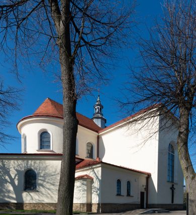 Zdjęcie nr 22: Kościół murowany, orientowany, jednonawowy, z transeptem, prezbiterium z obejściem i przybudówkami. Od zachodu kruchta, od północy kwadratowa kaplica, od południa kolejna przybudówka. 
Prezbiterium zamknięte półokrągło, z obejściem przeprutym do niego arkadami wspartymi na filarach. Ściany nawy i prezbiterium gładkie, przekryte sklepieniem kolebkowym z lunetami, w których mieszczą się okna. Transept i przecięcie naw sklepione krzyżowo. Na ścianach polichromia figuralna ze scenami z Nowego Testamentu, w partii sklepienia drobne, złote gwiazdki. Od zachodu chór zatopiony w występującym asymetrycznie murze, z tralkową balustradą. W prezbiterium siedem okien w kształcie stojącego prostokąta zamkniętego łukiem pełnym wypełnionych witrażami, w nawie sześć okien, w ramionach transeptu po jednym, czterodzielnym, wypełnionym witrażem, na wysokości chóru po dwa z każdej strony. Główne wejście od zachodu przez kruchtę. Fasada poprzedzona przedsionkiem o podziałach ramowych, z prostokątnym wejściem na osi, flankowanym parą pilastrów i prostokątnymi płycinami. Kondygnację wieńczy pełne belkowanie z wysuniętym gzymsem podtrzymującym daszek i trójkątny, schodkowy szczyt zakończony postumentami. Na centralnym krzyż, na sąsiadujących figury dzieci z rogami obfitości, a na zewnętrznych wazony płomieniste; szczyt ujmują postumenty z kulami. Fasada dwukondygnacyjna ze szczytem. Kondygnacja trójosiowa, rozdzielona pilastrami, o polach wypełnionych blendami w kształcie stojących prostokątów zamkniętych łukiem pełnym; szczyt trójkątny, z tarczą zegarową pośrodku. Budynek kościoła o wyraźnych podziałach na bryły składowe, ściany gładkie, przeprute oknami, z gzymsami pod krawędziami dachu. 
Nad nawą główną, na kalenicy, wieżyczka na sygnaturkę z latarnią i baniastym hełmem, druga na skrzyżowaniu naw, z latarnią i  hełmem zakończonym krzyżem. Dach nad nawą główną i przedsionkiem dwuspadowy, nad ramionami transeptu trójspadowym,nad prezbiterium zakończony wielobocznie, na przybudówkach dachy pulpitowe, dwuspadowe i wielospadowe. Dachy kryte dachówką ceramiczną, wieżyczki blachą. 
Najciekawszymi zabytkami kościoła są ołtarz główny z około 1700 roku z nastawą utworzoną z wici winnej latorośli, manierystyczny ołtarz boczny oraz siedemnastowieczna chrzcielnica z warsztatu Santi Gucciego. 
