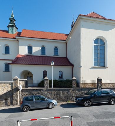 Zdjęcie nr 28: Kościół murowany, orientowany, jednonawowy, z transeptem, prezbiterium z obejściem i przybudówkami. Od zachodu kruchta, od północy kwadratowa kaplica, od południa kolejna przybudówka. 
Prezbiterium zamknięte półokrągło, z obejściem przeprutym do niego arkadami wspartymi na filarach. Ściany nawy i prezbiterium gładkie, przekryte sklepieniem kolebkowym z lunetami, w których mieszczą się okna. Transept i przecięcie naw sklepione krzyżowo. Na ścianach polichromia figuralna ze scenami z Nowego Testamentu, w partii sklepienia drobne, złote gwiazdki. Od zachodu chór zatopiony w występującym asymetrycznie murze, z tralkową balustradą. W prezbiterium siedem okien w kształcie stojącego prostokąta zamkniętego łukiem pełnym wypełnionych witrażami, w nawie sześć okien, w ramionach transeptu po jednym, czterodzielnym, wypełnionym witrażem, na wysokości chóru po dwa z każdej strony. Główne wejście od zachodu przez kruchtę. Fasada poprzedzona przedsionkiem o podziałach ramowych, z prostokątnym wejściem na osi, flankowanym parą pilastrów i prostokątnymi płycinami. Kondygnację wieńczy pełne belkowanie z wysuniętym gzymsem podtrzymującym daszek i trójkątny, schodkowy szczyt zakończony postumentami. Na centralnym krzyż, na sąsiadujących figury dzieci z rogami obfitości, a na zewnętrznych wazony płomieniste; szczyt ujmują postumenty z kulami. Fasada dwukondygnacyjna ze szczytem. Kondygnacja trójosiowa, rozdzielona pilastrami, o polach wypełnionych blendami w kształcie stojących prostokątów zamkniętych łukiem pełnym; szczyt trójkątny, z tarczą zegarową pośrodku. Budynek kościoła o wyraźnych podziałach na bryły składowe, ściany gładkie, przeprute oknami, z gzymsami pod krawędziami dachu. 
Nad nawą główną, na kalenicy, wieżyczka na sygnaturkę z latarnią i baniastym hełmem, druga na skrzyżowaniu naw, z latarnią i  hełmem zakończonym krzyżem. Dach nad nawą główną i przedsionkiem dwuspadowy, nad ramionami transeptu trójspadowym,nad prezbiterium zakończony wielobocznie, na przybudówkach dachy pulpitowe, dwuspadowe i wielospadowe. Dachy kryte dachówką ceramiczną, wieżyczki blachą. 
Najciekawszymi zabytkami kościoła są ołtarz główny z około 1700 roku z nastawą utworzoną z wici winnej latorośli, manierystyczny ołtarz boczny oraz siedemnastowieczna chrzcielnica z warsztatu Santi Gucciego. 
