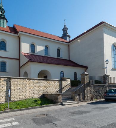 Zdjęcie nr 30: Kościół murowany, orientowany, jednonawowy, z transeptem, prezbiterium z obejściem i przybudówkami. Od zachodu kruchta, od północy kwadratowa kaplica, od południa kolejna przybudówka. 
Prezbiterium zamknięte półokrągło, z obejściem przeprutym do niego arkadami wspartymi na filarach. Ściany nawy i prezbiterium gładkie, przekryte sklepieniem kolebkowym z lunetami, w których mieszczą się okna. Transept i przecięcie naw sklepione krzyżowo. Na ścianach polichromia figuralna ze scenami z Nowego Testamentu, w partii sklepienia drobne, złote gwiazdki. Od zachodu chór zatopiony w występującym asymetrycznie murze, z tralkową balustradą. W prezbiterium siedem okien w kształcie stojącego prostokąta zamkniętego łukiem pełnym wypełnionych witrażami, w nawie sześć okien, w ramionach transeptu po jednym, czterodzielnym, wypełnionym witrażem, na wysokości chóru po dwa z każdej strony. Główne wejście od zachodu przez kruchtę. Fasada poprzedzona przedsionkiem o podziałach ramowych, z prostokątnym wejściem na osi, flankowanym parą pilastrów i prostokątnymi płycinami. Kondygnację wieńczy pełne belkowanie z wysuniętym gzymsem podtrzymującym daszek i trójkątny, schodkowy szczyt zakończony postumentami. Na centralnym krzyż, na sąsiadujących figury dzieci z rogami obfitości, a na zewnętrznych wazony płomieniste; szczyt ujmują postumenty z kulami. Fasada dwukondygnacyjna ze szczytem. Kondygnacja trójosiowa, rozdzielona pilastrami, o polach wypełnionych blendami w kształcie stojących prostokątów zamkniętych łukiem pełnym; szczyt trójkątny, z tarczą zegarową pośrodku. Budynek kościoła o wyraźnych podziałach na bryły składowe, ściany gładkie, przeprute oknami, z gzymsami pod krawędziami dachu. 
Nad nawą główną, na kalenicy, wieżyczka na sygnaturkę z latarnią i baniastym hełmem, druga na skrzyżowaniu naw, z latarnią i  hełmem zakończonym krzyżem. Dach nad nawą główną i przedsionkiem dwuspadowy, nad ramionami transeptu trójspadowym,nad prezbiterium zakończony wielobocznie, na przybudówkach dachy pulpitowe, dwuspadowe i wielospadowe. Dachy kryte dachówką ceramiczną, wieżyczki blachą. 
Najciekawszymi zabytkami kościoła są ołtarz główny z około 1700 roku z nastawą utworzoną z wici winnej latorośli, manierystyczny ołtarz boczny oraz siedemnastowieczna chrzcielnica z warsztatu Santi Gucciego. 
