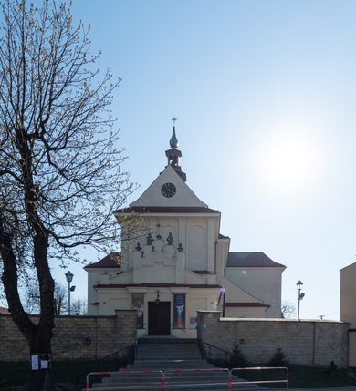 Zdjęcie nr 31: Kościół murowany, orientowany, jednonawowy, z transeptem, prezbiterium z obejściem i przybudówkami. Od zachodu kruchta, od północy kwadratowa kaplica, od południa kolejna przybudówka. 
Prezbiterium zamknięte półokrągło, z obejściem przeprutym do niego arkadami wspartymi na filarach. Ściany nawy i prezbiterium gładkie, przekryte sklepieniem kolebkowym z lunetami, w których mieszczą się okna. Transept i przecięcie naw sklepione krzyżowo. Na ścianach polichromia figuralna ze scenami z Nowego Testamentu, w partii sklepienia drobne, złote gwiazdki. Od zachodu chór zatopiony w występującym asymetrycznie murze, z tralkową balustradą. W prezbiterium siedem okien w kształcie stojącego prostokąta zamkniętego łukiem pełnym wypełnionych witrażami, w nawie sześć okien, w ramionach transeptu po jednym, czterodzielnym, wypełnionym witrażem, na wysokości chóru po dwa z każdej strony. Główne wejście od zachodu przez kruchtę. Fasada poprzedzona przedsionkiem o podziałach ramowych, z prostokątnym wejściem na osi, flankowanym parą pilastrów i prostokątnymi płycinami. Kondygnację wieńczy pełne belkowanie z wysuniętym gzymsem podtrzymującym daszek i trójkątny, schodkowy szczyt zakończony postumentami. Na centralnym krzyż, na sąsiadujących figury dzieci z rogami obfitości, a na zewnętrznych wazony płomieniste; szczyt ujmują postumenty z kulami. Fasada dwukondygnacyjna ze szczytem. Kondygnacja trójosiowa, rozdzielona pilastrami, o polach wypełnionych blendami w kształcie stojących prostokątów zamkniętych łukiem pełnym; szczyt trójkątny, z tarczą zegarową pośrodku. Budynek kościoła o wyraźnych podziałach na bryły składowe, ściany gładkie, przeprute oknami, z gzymsami pod krawędziami dachu. 
Nad nawą główną, na kalenicy, wieżyczka na sygnaturkę z latarnią i baniastym hełmem, druga na skrzyżowaniu naw, z latarnią i  hełmem zakończonym krzyżem. Dach nad nawą główną i przedsionkiem dwuspadowy, nad ramionami transeptu trójspadowym,nad prezbiterium zakończony wielobocznie, na przybudówkach dachy pulpitowe, dwuspadowe i wielospadowe. Dachy kryte dachówką ceramiczną, wieżyczki blachą. 
Najciekawszymi zabytkami kościoła są ołtarz główny z około 1700 roku z nastawą utworzoną z wici winnej latorośli, manierystyczny ołtarz boczny oraz siedemnastowieczna chrzcielnica z warsztatu Santi Gucciego. 
