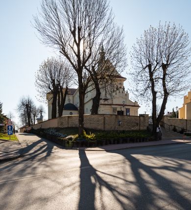 Zdjęcie nr 34: Kościół murowany, orientowany, jednonawowy, z transeptem, prezbiterium z obejściem i przybudówkami. Od zachodu kruchta, od północy kwadratowa kaplica, od południa kolejna przybudówka. 
Prezbiterium zamknięte półokrągło, z obejściem przeprutym do niego arkadami wspartymi na filarach. Ściany nawy i prezbiterium gładkie, przekryte sklepieniem kolebkowym z lunetami, w których mieszczą się okna. Transept i przecięcie naw sklepione krzyżowo. Na ścianach polichromia figuralna ze scenami z Nowego Testamentu, w partii sklepienia drobne, złote gwiazdki. Od zachodu chór zatopiony w występującym asymetrycznie murze, z tralkową balustradą. W prezbiterium siedem okien w kształcie stojącego prostokąta zamkniętego łukiem pełnym wypełnionych witrażami, w nawie sześć okien, w ramionach transeptu po jednym, czterodzielnym, wypełnionym witrażem, na wysokości chóru po dwa z każdej strony. Główne wejście od zachodu przez kruchtę. Fasada poprzedzona przedsionkiem o podziałach ramowych, z prostokątnym wejściem na osi, flankowanym parą pilastrów i prostokątnymi płycinami. Kondygnację wieńczy pełne belkowanie z wysuniętym gzymsem podtrzymującym daszek i trójkątny, schodkowy szczyt zakończony postumentami. Na centralnym krzyż, na sąsiadujących figury dzieci z rogami obfitości, a na zewnętrznych wazony płomieniste; szczyt ujmują postumenty z kulami. Fasada dwukondygnacyjna ze szczytem. Kondygnacja trójosiowa, rozdzielona pilastrami, o polach wypełnionych blendami w kształcie stojących prostokątów zamkniętych łukiem pełnym; szczyt trójkątny, z tarczą zegarową pośrodku. Budynek kościoła o wyraźnych podziałach na bryły składowe, ściany gładkie, przeprute oknami, z gzymsami pod krawędziami dachu. 
Nad nawą główną, na kalenicy, wieżyczka na sygnaturkę z latarnią i baniastym hełmem, druga na skrzyżowaniu naw, z latarnią i  hełmem zakończonym krzyżem. Dach nad nawą główną i przedsionkiem dwuspadowy, nad ramionami transeptu trójspadowym,nad prezbiterium zakończony wielobocznie, na przybudówkach dachy pulpitowe, dwuspadowe i wielospadowe. Dachy kryte dachówką ceramiczną, wieżyczki blachą. 
Najciekawszymi zabytkami kościoła są ołtarz główny z około 1700 roku z nastawą utworzoną z wici winnej latorośli, manierystyczny ołtarz boczny oraz siedemnastowieczna chrzcielnica z warsztatu Santi Gucciego. 
