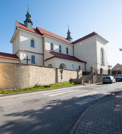 Zdjęcie nr 39: Kościół murowany, orientowany, jednonawowy, z transeptem, prezbiterium z obejściem i przybudówkami. Od zachodu kruchta, od północy kwadratowa kaplica, od południa kolejna przybudówka. 
Prezbiterium zamknięte półokrągło, z obejściem przeprutym do niego arkadami wspartymi na filarach. Ściany nawy i prezbiterium gładkie, przekryte sklepieniem kolebkowym z lunetami, w których mieszczą się okna. Transept i przecięcie naw sklepione krzyżowo. Na ścianach polichromia figuralna ze scenami z Nowego Testamentu, w partii sklepienia drobne, złote gwiazdki. Od zachodu chór zatopiony w występującym asymetrycznie murze, z tralkową balustradą. W prezbiterium siedem okien w kształcie stojącego prostokąta zamkniętego łukiem pełnym wypełnionych witrażami, w nawie sześć okien, w ramionach transeptu po jednym, czterodzielnym, wypełnionym witrażem, na wysokości chóru po dwa z każdej strony. Główne wejście od zachodu przez kruchtę. Fasada poprzedzona przedsionkiem o podziałach ramowych, z prostokątnym wejściem na osi, flankowanym parą pilastrów i prostokątnymi płycinami. Kondygnację wieńczy pełne belkowanie z wysuniętym gzymsem podtrzymującym daszek i trójkątny, schodkowy szczyt zakończony postumentami. Na centralnym krzyż, na sąsiadujących figury dzieci z rogami obfitości, a na zewnętrznych wazony płomieniste; szczyt ujmują postumenty z kulami. Fasada dwukondygnacyjna ze szczytem. Kondygnacja trójosiowa, rozdzielona pilastrami, o polach wypełnionych blendami w kształcie stojących prostokątów zamkniętych łukiem pełnym; szczyt trójkątny, z tarczą zegarową pośrodku. Budynek kościoła o wyraźnych podziałach na bryły składowe, ściany gładkie, przeprute oknami, z gzymsami pod krawędziami dachu. 
Nad nawą główną, na kalenicy, wieżyczka na sygnaturkę z latarnią i baniastym hełmem, druga na skrzyżowaniu naw, z latarnią i  hełmem zakończonym krzyżem. Dach nad nawą główną i przedsionkiem dwuspadowy, nad ramionami transeptu trójspadowym,nad prezbiterium zakończony wielobocznie, na przybudówkach dachy pulpitowe, dwuspadowe i wielospadowe. Dachy kryte dachówką ceramiczną, wieżyczki blachą. 
Najciekawszymi zabytkami kościoła są ołtarz główny z około 1700 roku z nastawą utworzoną z wici winnej latorośli, manierystyczny ołtarz boczny oraz siedemnastowieczna chrzcielnica z warsztatu Santi Gucciego. 
