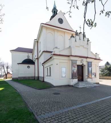 Zdjęcie nr 47: Kościół murowany, orientowany, jednonawowy, z transeptem, prezbiterium z obejściem i przybudówkami. Od zachodu kruchta, od północy kwadratowa kaplica, od południa kolejna przybudówka. 
Prezbiterium zamknięte półokrągło, z obejściem przeprutym do niego arkadami wspartymi na filarach. Ściany nawy i prezbiterium gładkie, przekryte sklepieniem kolebkowym z lunetami, w których mieszczą się okna. Transept i przecięcie naw sklepione krzyżowo. Na ścianach polichromia figuralna ze scenami z Nowego Testamentu, w partii sklepienia drobne, złote gwiazdki. Od zachodu chór zatopiony w występującym asymetrycznie murze, z tralkową balustradą. W prezbiterium siedem okien w kształcie stojącego prostokąta zamkniętego łukiem pełnym wypełnionych witrażami, w nawie sześć okien, w ramionach transeptu po jednym, czterodzielnym, wypełnionym witrażem, na wysokości chóru po dwa z każdej strony. Główne wejście od zachodu przez kruchtę. Fasada poprzedzona przedsionkiem o podziałach ramowych, z prostokątnym wejściem na osi, flankowanym parą pilastrów i prostokątnymi płycinami. Kondygnację wieńczy pełne belkowanie z wysuniętym gzymsem podtrzymującym daszek i trójkątny, schodkowy szczyt zakończony postumentami. Na centralnym krzyż, na sąsiadujących figury dzieci z rogami obfitości, a na zewnętrznych wazony płomieniste; szczyt ujmują postumenty z kulami. Fasada dwukondygnacyjna ze szczytem. Kondygnacja trójosiowa, rozdzielona pilastrami, o polach wypełnionych blendami w kształcie stojących prostokątów zamkniętych łukiem pełnym; szczyt trójkątny, z tarczą zegarową pośrodku. Budynek kościoła o wyraźnych podziałach na bryły składowe, ściany gładkie, przeprute oknami, z gzymsami pod krawędziami dachu. 
Nad nawą główną, na kalenicy, wieżyczka na sygnaturkę z latarnią i baniastym hełmem, druga na skrzyżowaniu naw, z latarnią i  hełmem zakończonym krzyżem. Dach nad nawą główną i przedsionkiem dwuspadowy, nad ramionami transeptu trójspadowym,nad prezbiterium zakończony wielobocznie, na przybudówkach dachy pulpitowe, dwuspadowe i wielospadowe. Dachy kryte dachówką ceramiczną, wieżyczki blachą. 
Najciekawszymi zabytkami kościoła są ołtarz główny z około 1700 roku z nastawą utworzoną z wici winnej latorośli, manierystyczny ołtarz boczny oraz siedemnastowieczna chrzcielnica z warsztatu Santi Gucciego. 
