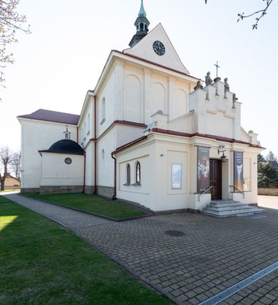 Zdjęcie nr 44: Kościół murowany, orientowany, jednonawowy, z transeptem, prezbiterium z obejściem i przybudówkami. Od zachodu kruchta, od północy kwadratowa kaplica, od południa kolejna przybudówka. 
Prezbiterium zamknięte półokrągło, z obejściem przeprutym do niego arkadami wspartymi na filarach. Ściany nawy i prezbiterium gładkie, przekryte sklepieniem kolebkowym z lunetami, w których mieszczą się okna. Transept i przecięcie naw sklepione krzyżowo. Na ścianach polichromia figuralna ze scenami z Nowego Testamentu, w partii sklepienia drobne, złote gwiazdki. Od zachodu chór zatopiony w występującym asymetrycznie murze, z tralkową balustradą. W prezbiterium siedem okien w kształcie stojącego prostokąta zamkniętego łukiem pełnym wypełnionych witrażami, w nawie sześć okien, w ramionach transeptu po jednym, czterodzielnym, wypełnionym witrażem, na wysokości chóru po dwa z każdej strony. Główne wejście od zachodu przez kruchtę. Fasada poprzedzona przedsionkiem o podziałach ramowych, z prostokątnym wejściem na osi, flankowanym parą pilastrów i prostokątnymi płycinami. Kondygnację wieńczy pełne belkowanie z wysuniętym gzymsem podtrzymującym daszek i trójkątny, schodkowy szczyt zakończony postumentami. Na centralnym krzyż, na sąsiadujących figury dzieci z rogami obfitości, a na zewnętrznych wazony płomieniste; szczyt ujmują postumenty z kulami. Fasada dwukondygnacyjna ze szczytem. Kondygnacja trójosiowa, rozdzielona pilastrami, o polach wypełnionych blendami w kształcie stojących prostokątów zamkniętych łukiem pełnym; szczyt trójkątny, z tarczą zegarową pośrodku. Budynek kościoła o wyraźnych podziałach na bryły składowe, ściany gładkie, przeprute oknami, z gzymsami pod krawędziami dachu. 
Nad nawą główną, na kalenicy, wieżyczka na sygnaturkę z latarnią i baniastym hełmem, druga na skrzyżowaniu naw, z latarnią i  hełmem zakończonym krzyżem. Dach nad nawą główną i przedsionkiem dwuspadowy, nad ramionami transeptu trójspadowym,nad prezbiterium zakończony wielobocznie, na przybudówkach dachy pulpitowe, dwuspadowe i wielospadowe. Dachy kryte dachówką ceramiczną, wieżyczki blachą. 
Najciekawszymi zabytkami kościoła są ołtarz główny z około 1700 roku z nastawą utworzoną z wici winnej latorośli, manierystyczny ołtarz boczny oraz siedemnastowieczna chrzcielnica z warsztatu Santi Gucciego. 
