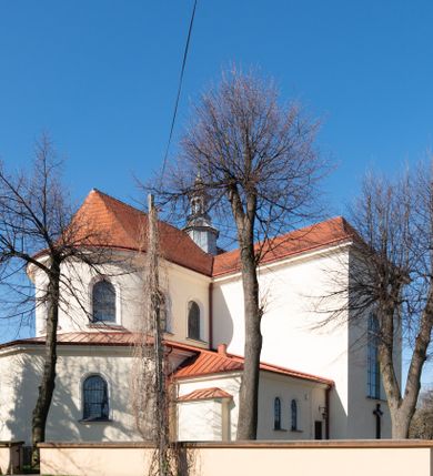 Zdjęcie nr 45: Kościół murowany, orientowany, jednonawowy, z transeptem, prezbiterium z obejściem i przybudówkami. Od zachodu kruchta, od północy kwadratowa kaplica, od południa kolejna przybudówka. 
Prezbiterium zamknięte półokrągło, z obejściem przeprutym do niego arkadami wspartymi na filarach. Ściany nawy i prezbiterium gładkie, przekryte sklepieniem kolebkowym z lunetami, w których mieszczą się okna. Transept i przecięcie naw sklepione krzyżowo. Na ścianach polichromia figuralna ze scenami z Nowego Testamentu, w partii sklepienia drobne, złote gwiazdki. Od zachodu chór zatopiony w występującym asymetrycznie murze, z tralkową balustradą. W prezbiterium siedem okien w kształcie stojącego prostokąta zamkniętego łukiem pełnym wypełnionych witrażami, w nawie sześć okien, w ramionach transeptu po jednym, czterodzielnym, wypełnionym witrażem, na wysokości chóru po dwa z każdej strony. Główne wejście od zachodu przez kruchtę. Fasada poprzedzona przedsionkiem o podziałach ramowych, z prostokątnym wejściem na osi, flankowanym parą pilastrów i prostokątnymi płycinami. Kondygnację wieńczy pełne belkowanie z wysuniętym gzymsem podtrzymującym daszek i trójkątny, schodkowy szczyt zakończony postumentami. Na centralnym krzyż, na sąsiadujących figury dzieci z rogami obfitości, a na zewnętrznych wazony płomieniste; szczyt ujmują postumenty z kulami. Fasada dwukondygnacyjna ze szczytem. Kondygnacja trójosiowa, rozdzielona pilastrami, o polach wypełnionych blendami w kształcie stojących prostokątów zamkniętych łukiem pełnym; szczyt trójkątny, z tarczą zegarową pośrodku. Budynek kościoła o wyraźnych podziałach na bryły składowe, ściany gładkie, przeprute oknami, z gzymsami pod krawędziami dachu. 
Nad nawą główną, na kalenicy, wieżyczka na sygnaturkę z latarnią i baniastym hełmem, druga na skrzyżowaniu naw, z latarnią i  hełmem zakończonym krzyżem. Dach nad nawą główną i przedsionkiem dwuspadowy, nad ramionami transeptu trójspadowym,nad prezbiterium zakończony wielobocznie, na przybudówkach dachy pulpitowe, dwuspadowe i wielospadowe. Dachy kryte dachówką ceramiczną, wieżyczki blachą. 
Najciekawszymi zabytkami kościoła są ołtarz główny z około 1700 roku z nastawą utworzoną z wici winnej latorośli, manierystyczny ołtarz boczny oraz siedemnastowieczna chrzcielnica z warsztatu Santi Gucciego. 
