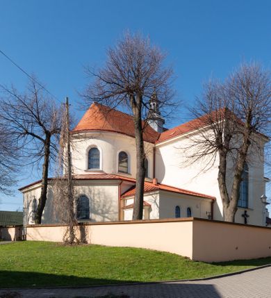 Zdjęcie nr 48: Kościół murowany, orientowany, jednonawowy, z transeptem, prezbiterium z obejściem i przybudówkami. Od zachodu kruchta, od północy kwadratowa kaplica, od południa kolejna przybudówka. 
Prezbiterium zamknięte półokrągło, z obejściem przeprutym do niego arkadami wspartymi na filarach. Ściany nawy i prezbiterium gładkie, przekryte sklepieniem kolebkowym z lunetami, w których mieszczą się okna. Transept i przecięcie naw sklepione krzyżowo. Na ścianach polichromia figuralna ze scenami z Nowego Testamentu, w partii sklepienia drobne, złote gwiazdki. Od zachodu chór zatopiony w występującym asymetrycznie murze, z tralkową balustradą. W prezbiterium siedem okien w kształcie stojącego prostokąta zamkniętego łukiem pełnym wypełnionych witrażami, w nawie sześć okien, w ramionach transeptu po jednym, czterodzielnym, wypełnionym witrażem, na wysokości chóru po dwa z każdej strony. Główne wejście od zachodu przez kruchtę. Fasada poprzedzona przedsionkiem o podziałach ramowych, z prostokątnym wejściem na osi, flankowanym parą pilastrów i prostokątnymi płycinami. Kondygnację wieńczy pełne belkowanie z wysuniętym gzymsem podtrzymującym daszek i trójkątny, schodkowy szczyt zakończony postumentami. Na centralnym krzyż, na sąsiadujących figury dzieci z rogami obfitości, a na zewnętrznych wazony płomieniste; szczyt ujmują postumenty z kulami. Fasada dwukondygnacyjna ze szczytem. Kondygnacja trójosiowa, rozdzielona pilastrami, o polach wypełnionych blendami w kształcie stojących prostokątów zamkniętych łukiem pełnym; szczyt trójkątny, z tarczą zegarową pośrodku. Budynek kościoła o wyraźnych podziałach na bryły składowe, ściany gładkie, przeprute oknami, z gzymsami pod krawędziami dachu. 
Nad nawą główną, na kalenicy, wieżyczka na sygnaturkę z latarnią i baniastym hełmem, druga na skrzyżowaniu naw, z latarnią i  hełmem zakończonym krzyżem. Dach nad nawą główną i przedsionkiem dwuspadowy, nad ramionami transeptu trójspadowym,nad prezbiterium zakończony wielobocznie, na przybudówkach dachy pulpitowe, dwuspadowe i wielospadowe. Dachy kryte dachówką ceramiczną, wieżyczki blachą. 
Najciekawszymi zabytkami kościoła są ołtarz główny z około 1700 roku z nastawą utworzoną z wici winnej latorośli, manierystyczny ołtarz boczny oraz siedemnastowieczna chrzcielnica z warsztatu Santi Gucciego. 
