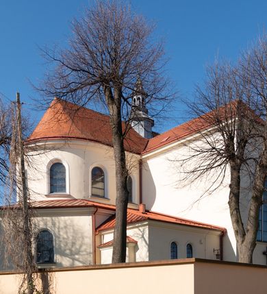 Zdjęcie nr 49: Kościół murowany, orientowany, jednonawowy, z transeptem, prezbiterium z obejściem i przybudówkami. Od zachodu kruchta, od północy kwadratowa kaplica, od południa kolejna przybudówka. 
Prezbiterium zamknięte półokrągło, z obejściem przeprutym do niego arkadami wspartymi na filarach. Ściany nawy i prezbiterium gładkie, przekryte sklepieniem kolebkowym z lunetami, w których mieszczą się okna. Transept i przecięcie naw sklepione krzyżowo. Na ścianach polichromia figuralna ze scenami z Nowego Testamentu, w partii sklepienia drobne, złote gwiazdki. Od zachodu chór zatopiony w występującym asymetrycznie murze, z tralkową balustradą. W prezbiterium siedem okien w kształcie stojącego prostokąta zamkniętego łukiem pełnym wypełnionych witrażami, w nawie sześć okien, w ramionach transeptu po jednym, czterodzielnym, wypełnionym witrażem, na wysokości chóru po dwa z każdej strony. Główne wejście od zachodu przez kruchtę. Fasada poprzedzona przedsionkiem o podziałach ramowych, z prostokątnym wejściem na osi, flankowanym parą pilastrów i prostokątnymi płycinami. Kondygnację wieńczy pełne belkowanie z wysuniętym gzymsem podtrzymującym daszek i trójkątny, schodkowy szczyt zakończony postumentami. Na centralnym krzyż, na sąsiadujących figury dzieci z rogami obfitości, a na zewnętrznych wazony płomieniste; szczyt ujmują postumenty z kulami. Fasada dwukondygnacyjna ze szczytem. Kondygnacja trójosiowa, rozdzielona pilastrami, o polach wypełnionych blendami w kształcie stojących prostokątów zamkniętych łukiem pełnym; szczyt trójkątny, z tarczą zegarową pośrodku. Budynek kościoła o wyraźnych podziałach na bryły składowe, ściany gładkie, przeprute oknami, z gzymsami pod krawędziami dachu. 
Nad nawą główną, na kalenicy, wieżyczka na sygnaturkę z latarnią i baniastym hełmem, druga na skrzyżowaniu naw, z latarnią i  hełmem zakończonym krzyżem. Dach nad nawą główną i przedsionkiem dwuspadowy, nad ramionami transeptu trójspadowym,nad prezbiterium zakończony wielobocznie, na przybudówkach dachy pulpitowe, dwuspadowe i wielospadowe. Dachy kryte dachówką ceramiczną, wieżyczki blachą. 
Najciekawszymi zabytkami kościoła są ołtarz główny z około 1700 roku z nastawą utworzoną z wici winnej latorośli, manierystyczny ołtarz boczny oraz siedemnastowieczna chrzcielnica z warsztatu Santi Gucciego. 
