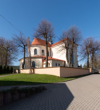 Zdjęcie nr 51: Kościół murowany, orientowany, jednonawowy, z transeptem, prezbiterium z obejściem i przybudówkami. Od zachodu kruchta, od północy kwadratowa kaplica, od południa kolejna przybudówka. 
Prezbiterium zamknięte półokrągło, z obejściem przeprutym do niego arkadami wspartymi na filarach. Ściany nawy i prezbiterium gładkie, przekryte sklepieniem kolebkowym z lunetami, w których mieszczą się okna. Transept i przecięcie naw sklepione krzyżowo. Na ścianach polichromia figuralna ze scenami z Nowego Testamentu, w partii sklepienia drobne, złote gwiazdki. Od zachodu chór zatopiony w występującym asymetrycznie murze, z tralkową balustradą. W prezbiterium siedem okien w kształcie stojącego prostokąta zamkniętego łukiem pełnym wypełnionych witrażami, w nawie sześć okien, w ramionach transeptu po jednym, czterodzielnym, wypełnionym witrażem, na wysokości chóru po dwa z każdej strony. Główne wejście od zachodu przez kruchtę. Fasada poprzedzona przedsionkiem o podziałach ramowych, z prostokątnym wejściem na osi, flankowanym parą pilastrów i prostokątnymi płycinami. Kondygnację wieńczy pełne belkowanie z wysuniętym gzymsem podtrzymującym daszek i trójkątny, schodkowy szczyt zakończony postumentami. Na centralnym krzyż, na sąsiadujących figury dzieci z rogami obfitości, a na zewnętrznych wazony płomieniste; szczyt ujmują postumenty z kulami. Fasada dwukondygnacyjna ze szczytem. Kondygnacja trójosiowa, rozdzielona pilastrami, o polach wypełnionych blendami w kształcie stojących prostokątów zamkniętych łukiem pełnym; szczyt trójkątny, z tarczą zegarową pośrodku. Budynek kościoła o wyraźnych podziałach na bryły składowe, ściany gładkie, przeprute oknami, z gzymsami pod krawędziami dachu. 
Nad nawą główną, na kalenicy, wieżyczka na sygnaturkę z latarnią i baniastym hełmem, druga na skrzyżowaniu naw, z latarnią i  hełmem zakończonym krzyżem. Dach nad nawą główną i przedsionkiem dwuspadowy, nad ramionami transeptu trójspadowym,nad prezbiterium zakończony wielobocznie, na przybudówkach dachy pulpitowe, dwuspadowe i wielospadowe. Dachy kryte dachówką ceramiczną, wieżyczki blachą. 
Najciekawszymi zabytkami kościoła są ołtarz główny z około 1700 roku z nastawą utworzoną z wici winnej latorośli, manierystyczny ołtarz boczny oraz siedemnastowieczna chrzcielnica z warsztatu Santi Gucciego. 
