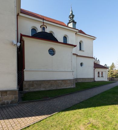 Zdjęcie nr 52: Kościół murowany, orientowany, jednonawowy, z transeptem, prezbiterium z obejściem i przybudówkami. Od zachodu kruchta, od północy kwadratowa kaplica, od południa kolejna przybudówka. 
Prezbiterium zamknięte półokrągło, z obejściem przeprutym do niego arkadami wspartymi na filarach. Ściany nawy i prezbiterium gładkie, przekryte sklepieniem kolebkowym z lunetami, w których mieszczą się okna. Transept i przecięcie naw sklepione krzyżowo. Na ścianach polichromia figuralna ze scenami z Nowego Testamentu, w partii sklepienia drobne, złote gwiazdki. Od zachodu chór zatopiony w występującym asymetrycznie murze, z tralkową balustradą. W prezbiterium siedem okien w kształcie stojącego prostokąta zamkniętego łukiem pełnym wypełnionych witrażami, w nawie sześć okien, w ramionach transeptu po jednym, czterodzielnym, wypełnionym witrażem, na wysokości chóru po dwa z każdej strony. Główne wejście od zachodu przez kruchtę. Fasada poprzedzona przedsionkiem o podziałach ramowych, z prostokątnym wejściem na osi, flankowanym parą pilastrów i prostokątnymi płycinami. Kondygnację wieńczy pełne belkowanie z wysuniętym gzymsem podtrzymującym daszek i trójkątny, schodkowy szczyt zakończony postumentami. Na centralnym krzyż, na sąsiadujących figury dzieci z rogami obfitości, a na zewnętrznych wazony płomieniste; szczyt ujmują postumenty z kulami. Fasada dwukondygnacyjna ze szczytem. Kondygnacja trójosiowa, rozdzielona pilastrami, o polach wypełnionych blendami w kształcie stojących prostokątów zamkniętych łukiem pełnym; szczyt trójkątny, z tarczą zegarową pośrodku. Budynek kościoła o wyraźnych podziałach na bryły składowe, ściany gładkie, przeprute oknami, z gzymsami pod krawędziami dachu. 
Nad nawą główną, na kalenicy, wieżyczka na sygnaturkę z latarnią i baniastym hełmem, druga na skrzyżowaniu naw, z latarnią i  hełmem zakończonym krzyżem. Dach nad nawą główną i przedsionkiem dwuspadowy, nad ramionami transeptu trójspadowym,nad prezbiterium zakończony wielobocznie, na przybudówkach dachy pulpitowe, dwuspadowe i wielospadowe. Dachy kryte dachówką ceramiczną, wieżyczki blachą. 
Najciekawszymi zabytkami kościoła są ołtarz główny z około 1700 roku z nastawą utworzoną z wici winnej latorośli, manierystyczny ołtarz boczny oraz siedemnastowieczna chrzcielnica z warsztatu Santi Gucciego. 
