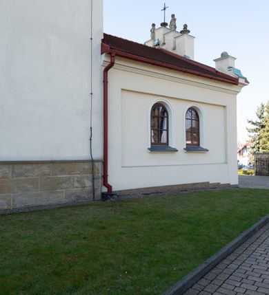 Zdjęcie nr 55: Kościół murowany, orientowany, jednonawowy, z transeptem, prezbiterium z obejściem i przybudówkami. Od zachodu kruchta, od północy kwadratowa kaplica, od południa kolejna przybudówka. 
Prezbiterium zamknięte półokrągło, z obejściem przeprutym do niego arkadami wspartymi na filarach. Ściany nawy i prezbiterium gładkie, przekryte sklepieniem kolebkowym z lunetami, w których mieszczą się okna. Transept i przecięcie naw sklepione krzyżowo. Na ścianach polichromia figuralna ze scenami z Nowego Testamentu, w partii sklepienia drobne, złote gwiazdki. Od zachodu chór zatopiony w występującym asymetrycznie murze, z tralkową balustradą. W prezbiterium siedem okien w kształcie stojącego prostokąta zamkniętego łukiem pełnym wypełnionych witrażami, w nawie sześć okien, w ramionach transeptu po jednym, czterodzielnym, wypełnionym witrażem, na wysokości chóru po dwa z każdej strony. Główne wejście od zachodu przez kruchtę. Fasada poprzedzona przedsionkiem o podziałach ramowych, z prostokątnym wejściem na osi, flankowanym parą pilastrów i prostokątnymi płycinami. Kondygnację wieńczy pełne belkowanie z wysuniętym gzymsem podtrzymującym daszek i trójkątny, schodkowy szczyt zakończony postumentami. Na centralnym krzyż, na sąsiadujących figury dzieci z rogami obfitości, a na zewnętrznych wazony płomieniste; szczyt ujmują postumenty z kulami. Fasada dwukondygnacyjna ze szczytem. Kondygnacja trójosiowa, rozdzielona pilastrami, o polach wypełnionych blendami w kształcie stojących prostokątów zamkniętych łukiem pełnym; szczyt trójkątny, z tarczą zegarową pośrodku. Budynek kościoła o wyraźnych podziałach na bryły składowe, ściany gładkie, przeprute oknami, z gzymsami pod krawędziami dachu. 
Nad nawą główną, na kalenicy, wieżyczka na sygnaturkę z latarnią i baniastym hełmem, druga na skrzyżowaniu naw, z latarnią i  hełmem zakończonym krzyżem. Dach nad nawą główną i przedsionkiem dwuspadowy, nad ramionami transeptu trójspadowym,nad prezbiterium zakończony wielobocznie, na przybudówkach dachy pulpitowe, dwuspadowe i wielospadowe. Dachy kryte dachówką ceramiczną, wieżyczki blachą. 
Najciekawszymi zabytkami kościoła są ołtarz główny z około 1700 roku z nastawą utworzoną z wici winnej latorośli, manierystyczny ołtarz boczny oraz siedemnastowieczna chrzcielnica z warsztatu Santi Gucciego. 
