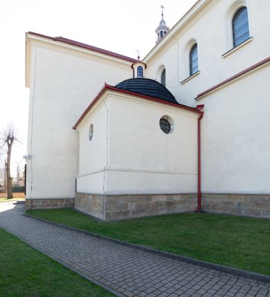 Zdjęcie nr 56: Kościół murowany, orientowany, jednonawowy, z transeptem, prezbiterium z obejściem i przybudówkami. Od zachodu kruchta, od północy kwadratowa kaplica, od południa kolejna przybudówka. 
Prezbiterium zamknięte półokrągło, z obejściem przeprutym do niego arkadami wspartymi na filarach. Ściany nawy i prezbiterium gładkie, przekryte sklepieniem kolebkowym z lunetami, w których mieszczą się okna. Transept i przecięcie naw sklepione krzyżowo. Na ścianach polichromia figuralna ze scenami z Nowego Testamentu, w partii sklepienia drobne, złote gwiazdki. Od zachodu chór zatopiony w występującym asymetrycznie murze, z tralkową balustradą. W prezbiterium siedem okien w kształcie stojącego prostokąta zamkniętego łukiem pełnym wypełnionych witrażami, w nawie sześć okien, w ramionach transeptu po jednym, czterodzielnym, wypełnionym witrażem, na wysokości chóru po dwa z każdej strony. Główne wejście od zachodu przez kruchtę. Fasada poprzedzona przedsionkiem o podziałach ramowych, z prostokątnym wejściem na osi, flankowanym parą pilastrów i prostokątnymi płycinami. Kondygnację wieńczy pełne belkowanie z wysuniętym gzymsem podtrzymującym daszek i trójkątny, schodkowy szczyt zakończony postumentami. Na centralnym krzyż, na sąsiadujących figury dzieci z rogami obfitości, a na zewnętrznych wazony płomieniste; szczyt ujmują postumenty z kulami. Fasada dwukondygnacyjna ze szczytem. Kondygnacja trójosiowa, rozdzielona pilastrami, o polach wypełnionych blendami w kształcie stojących prostokątów zamkniętych łukiem pełnym; szczyt trójkątny, z tarczą zegarową pośrodku. Budynek kościoła o wyraźnych podziałach na bryły składowe, ściany gładkie, przeprute oknami, z gzymsami pod krawędziami dachu. 
Nad nawą główną, na kalenicy, wieżyczka na sygnaturkę z latarnią i baniastym hełmem, druga na skrzyżowaniu naw, z latarnią i  hełmem zakończonym krzyżem. Dach nad nawą główną i przedsionkiem dwuspadowy, nad ramionami transeptu trójspadowym,nad prezbiterium zakończony wielobocznie, na przybudówkach dachy pulpitowe, dwuspadowe i wielospadowe. Dachy kryte dachówką ceramiczną, wieżyczki blachą. 
Najciekawszymi zabytkami kościoła są ołtarz główny z około 1700 roku z nastawą utworzoną z wici winnej latorośli, manierystyczny ołtarz boczny oraz siedemnastowieczna chrzcielnica z warsztatu Santi Gucciego. 
