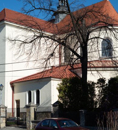 Zdjęcie nr 74: Kościół murowany, orientowany, jednonawowy, z transeptem, prezbiterium z obejściem i przybudówkami. Od zachodu kruchta, od północy kwadratowa kaplica, od południa kolejna przybudówka. 
Prezbiterium zamknięte półokrągło, z obejściem przeprutym do niego arkadami wspartymi na filarach. Ściany nawy i prezbiterium gładkie, przekryte sklepieniem kolebkowym z lunetami, w których mieszczą się okna. Transept i przecięcie naw sklepione krzyżowo. Na ścianach polichromia figuralna ze scenami z Nowego Testamentu, w partii sklepienia drobne, złote gwiazdki. Od zachodu chór zatopiony w występującym asymetrycznie murze, z tralkową balustradą. W prezbiterium siedem okien w kształcie stojącego prostokąta zamkniętego łukiem pełnym wypełnionych witrażami, w nawie sześć okien, w ramionach transeptu po jednym, czterodzielnym, wypełnionym witrażem, na wysokości chóru po dwa z każdej strony. Główne wejście od zachodu przez kruchtę. Fasada poprzedzona przedsionkiem o podziałach ramowych, z prostokątnym wejściem na osi, flankowanym parą pilastrów i prostokątnymi płycinami. Kondygnację wieńczy pełne belkowanie z wysuniętym gzymsem podtrzymującym daszek i trójkątny, schodkowy szczyt zakończony postumentami. Na centralnym krzyż, na sąsiadujących figury dzieci z rogami obfitości, a na zewnętrznych wazony płomieniste; szczyt ujmują postumenty z kulami. Fasada dwukondygnacyjna ze szczytem. Kondygnacja trójosiowa, rozdzielona pilastrami, o polach wypełnionych blendami w kształcie stojących prostokątów zamkniętych łukiem pełnym; szczyt trójkątny, z tarczą zegarową pośrodku. Budynek kościoła o wyraźnych podziałach na bryły składowe, ściany gładkie, przeprute oknami, z gzymsami pod krawędziami dachu. 
Nad nawą główną, na kalenicy, wieżyczka na sygnaturkę z latarnią i baniastym hełmem, druga na skrzyżowaniu naw, z latarnią i  hełmem zakończonym krzyżem. Dach nad nawą główną i przedsionkiem dwuspadowy, nad ramionami transeptu trójspadowym,nad prezbiterium zakończony wielobocznie, na przybudówkach dachy pulpitowe, dwuspadowe i wielospadowe. Dachy kryte dachówką ceramiczną, wieżyczki blachą. 
Najciekawszymi zabytkami kościoła są ołtarz główny z około 1700 roku z nastawą utworzoną z wici winnej latorośli, manierystyczny ołtarz boczny oraz siedemnastowieczna chrzcielnica z warsztatu Santi Gucciego. 
