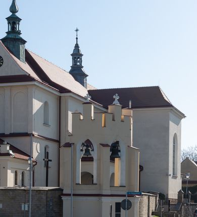 Zdjęcie nr 86: Kościół murowany, orientowany, jednonawowy, z transeptem, prezbiterium z obejściem i przybudówkami. Od zachodu kruchta, od północy kwadratowa kaplica, od południa kolejna przybudówka. 
Prezbiterium zamknięte półokrągło, z obejściem przeprutym do niego arkadami wspartymi na filarach. Ściany nawy i prezbiterium gładkie, przekryte sklepieniem kolebkowym z lunetami, w których mieszczą się okna. Transept i przecięcie naw sklepione krzyżowo. Na ścianach polichromia figuralna ze scenami z Nowego Testamentu, w partii sklepienia drobne, złote gwiazdki. Od zachodu chór zatopiony w występującym asymetrycznie murze, z tralkową balustradą. W prezbiterium siedem okien w kształcie stojącego prostokąta zamkniętego łukiem pełnym wypełnionych witrażami, w nawie sześć okien, w ramionach transeptu po jednym, czterodzielnym, wypełnionym witrażem, na wysokości chóru po dwa z każdej strony. Główne wejście od zachodu przez kruchtę. Fasada poprzedzona przedsionkiem o podziałach ramowych, z prostokątnym wejściem na osi, flankowanym parą pilastrów i prostokątnymi płycinami. Kondygnację wieńczy pełne belkowanie z wysuniętym gzymsem podtrzymującym daszek i trójkątny, schodkowy szczyt zakończony postumentami. Na centralnym krzyż, na sąsiadujących figury dzieci z rogami obfitości, a na zewnętrznych wazony płomieniste; szczyt ujmują postumenty z kulami. Fasada dwukondygnacyjna ze szczytem. Kondygnacja trójosiowa, rozdzielona pilastrami, o polach wypełnionych blendami w kształcie stojących prostokątów zamkniętych łukiem pełnym; szczyt trójkątny, z tarczą zegarową pośrodku. Budynek kościoła o wyraźnych podziałach na bryły składowe, ściany gładkie, przeprute oknami, z gzymsami pod krawędziami dachu. 
Nad nawą główną, na kalenicy, wieżyczka na sygnaturkę z latarnią i baniastym hełmem, druga na skrzyżowaniu naw, z latarnią i  hełmem zakończonym krzyżem. Dach nad nawą główną i przedsionkiem dwuspadowy, nad ramionami transeptu trójspadowym,nad prezbiterium zakończony wielobocznie, na przybudówkach dachy pulpitowe, dwuspadowe i wielospadowe. Dachy kryte dachówką ceramiczną, wieżyczki blachą. 
Najciekawszymi zabytkami kościoła są ołtarz główny z około 1700 roku z nastawą utworzoną z wici winnej latorośli, manierystyczny ołtarz boczny oraz siedemnastowieczna chrzcielnica z warsztatu Santi Gucciego. 
