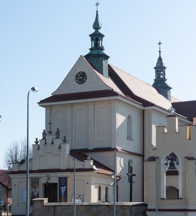 Zdjęcie nr 85: Kościół murowany, orientowany, jednonawowy, z transeptem, prezbiterium z obejściem i przybudówkami. Od zachodu kruchta, od północy kwadratowa kaplica, od południa kolejna przybudówka. 
Prezbiterium zamknięte półokrągło, z obejściem przeprutym do niego arkadami wspartymi na filarach. Ściany nawy i prezbiterium gładkie, przekryte sklepieniem kolebkowym z lunetami, w których mieszczą się okna. Transept i przecięcie naw sklepione krzyżowo. Na ścianach polichromia figuralna ze scenami z Nowego Testamentu, w partii sklepienia drobne, złote gwiazdki. Od zachodu chór zatopiony w występującym asymetrycznie murze, z tralkową balustradą. W prezbiterium siedem okien w kształcie stojącego prostokąta zamkniętego łukiem pełnym wypełnionych witrażami, w nawie sześć okien, w ramionach transeptu po jednym, czterodzielnym, wypełnionym witrażem, na wysokości chóru po dwa z każdej strony. Główne wejście od zachodu przez kruchtę. Fasada poprzedzona przedsionkiem o podziałach ramowych, z prostokątnym wejściem na osi, flankowanym parą pilastrów i prostokątnymi płycinami. Kondygnację wieńczy pełne belkowanie z wysuniętym gzymsem podtrzymującym daszek i trójkątny, schodkowy szczyt zakończony postumentami. Na centralnym krzyż, na sąsiadujących figury dzieci z rogami obfitości, a na zewnętrznych wazony płomieniste; szczyt ujmują postumenty z kulami. Fasada dwukondygnacyjna ze szczytem. Kondygnacja trójosiowa, rozdzielona pilastrami, o polach wypełnionych blendami w kształcie stojących prostokątów zamkniętych łukiem pełnym; szczyt trójkątny, z tarczą zegarową pośrodku. Budynek kościoła o wyraźnych podziałach na bryły składowe, ściany gładkie, przeprute oknami, z gzymsami pod krawędziami dachu. 
Nad nawą główną, na kalenicy, wieżyczka na sygnaturkę z latarnią i baniastym hełmem, druga na skrzyżowaniu naw, z latarnią i  hełmem zakończonym krzyżem. Dach nad nawą główną i przedsionkiem dwuspadowy, nad ramionami transeptu trójspadowym,nad prezbiterium zakończony wielobocznie, na przybudówkach dachy pulpitowe, dwuspadowe i wielospadowe. Dachy kryte dachówką ceramiczną, wieżyczki blachą. 
Najciekawszymi zabytkami kościoła są ołtarz główny z około 1700 roku z nastawą utworzoną z wici winnej latorośli, manierystyczny ołtarz boczny oraz siedemnastowieczna chrzcielnica z warsztatu Santi Gucciego. 
