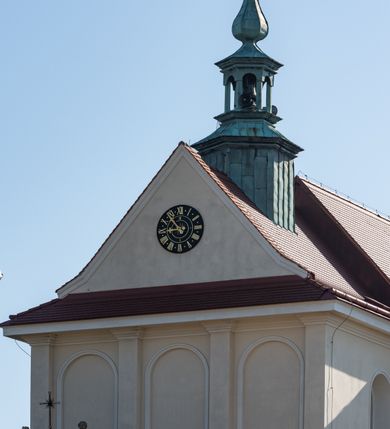 Zdjęcie nr 89: Kościół murowany, orientowany, jednonawowy, z transeptem, prezbiterium z obejściem i przybudówkami. Od zachodu kruchta, od północy kwadratowa kaplica, od południa kolejna przybudówka. 
Prezbiterium zamknięte półokrągło, z obejściem przeprutym do niego arkadami wspartymi na filarach. Ściany nawy i prezbiterium gładkie, przekryte sklepieniem kolebkowym z lunetami, w których mieszczą się okna. Transept i przecięcie naw sklepione krzyżowo. Na ścianach polichromia figuralna ze scenami z Nowego Testamentu, w partii sklepienia drobne, złote gwiazdki. Od zachodu chór zatopiony w występującym asymetrycznie murze, z tralkową balustradą. W prezbiterium siedem okien w kształcie stojącego prostokąta zamkniętego łukiem pełnym wypełnionych witrażami, w nawie sześć okien, w ramionach transeptu po jednym, czterodzielnym, wypełnionym witrażem, na wysokości chóru po dwa z każdej strony. Główne wejście od zachodu przez kruchtę. Fasada poprzedzona przedsionkiem o podziałach ramowych, z prostokątnym wejściem na osi, flankowanym parą pilastrów i prostokątnymi płycinami. Kondygnację wieńczy pełne belkowanie z wysuniętym gzymsem podtrzymującym daszek i trójkątny, schodkowy szczyt zakończony postumentami. Na centralnym krzyż, na sąsiadujących figury dzieci z rogami obfitości, a na zewnętrznych wazony płomieniste; szczyt ujmują postumenty z kulami. Fasada dwukondygnacyjna ze szczytem. Kondygnacja trójosiowa, rozdzielona pilastrami, o polach wypełnionych blendami w kształcie stojących prostokątów zamkniętych łukiem pełnym; szczyt trójkątny, z tarczą zegarową pośrodku. Budynek kościoła o wyraźnych podziałach na bryły składowe, ściany gładkie, przeprute oknami, z gzymsami pod krawędziami dachu. 
Nad nawą główną, na kalenicy, wieżyczka na sygnaturkę z latarnią i baniastym hełmem, druga na skrzyżowaniu naw, z latarnią i  hełmem zakończonym krzyżem. Dach nad nawą główną i przedsionkiem dwuspadowy, nad ramionami transeptu trójspadowym,nad prezbiterium zakończony wielobocznie, na przybudówkach dachy pulpitowe, dwuspadowe i wielospadowe. Dachy kryte dachówką ceramiczną, wieżyczki blachą. 
Najciekawszymi zabytkami kościoła są ołtarz główny z około 1700 roku z nastawą utworzoną z wici winnej latorośli, manierystyczny ołtarz boczny oraz siedemnastowieczna chrzcielnica z warsztatu Santi Gucciego. 
