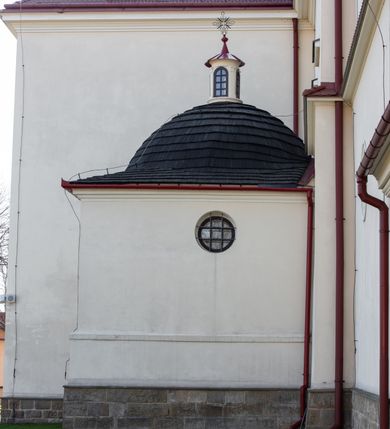 Zdjęcie nr 102: Kościół murowany, orientowany, jednonawowy, z transeptem, prezbiterium z obejściem i przybudówkami. Od zachodu kruchta, od północy kwadratowa kaplica, od południa kolejna przybudówka. 
Prezbiterium zamknięte półokrągło, z obejściem przeprutym do niego arkadami wspartymi na filarach. Ściany nawy i prezbiterium gładkie, przekryte sklepieniem kolebkowym z lunetami, w których mieszczą się okna. Transept i przecięcie naw sklepione krzyżowo. Na ścianach polichromia figuralna ze scenami z Nowego Testamentu, w partii sklepienia drobne, złote gwiazdki. Od zachodu chór zatopiony w występującym asymetrycznie murze, z tralkową balustradą. W prezbiterium siedem okien w kształcie stojącego prostokąta zamkniętego łukiem pełnym wypełnionych witrażami, w nawie sześć okien, w ramionach transeptu po jednym, czterodzielnym, wypełnionym witrażem, na wysokości chóru po dwa z każdej strony. Główne wejście od zachodu przez kruchtę. Fasada poprzedzona przedsionkiem o podziałach ramowych, z prostokątnym wejściem na osi, flankowanym parą pilastrów i prostokątnymi płycinami. Kondygnację wieńczy pełne belkowanie z wysuniętym gzymsem podtrzymującym daszek i trójkątny, schodkowy szczyt zakończony postumentami. Na centralnym krzyż, na sąsiadujących figury dzieci z rogami obfitości, a na zewnętrznych wazony płomieniste; szczyt ujmują postumenty z kulami. Fasada dwukondygnacyjna ze szczytem. Kondygnacja trójosiowa, rozdzielona pilastrami, o polach wypełnionych blendami w kształcie stojących prostokątów zamkniętych łukiem pełnym; szczyt trójkątny, z tarczą zegarową pośrodku. Budynek kościoła o wyraźnych podziałach na bryły składowe, ściany gładkie, przeprute oknami, z gzymsami pod krawędziami dachu. 
Nad nawą główną, na kalenicy, wieżyczka na sygnaturkę z latarnią i baniastym hełmem, druga na skrzyżowaniu naw, z latarnią i  hełmem zakończonym krzyżem. Dach nad nawą główną i przedsionkiem dwuspadowy, nad ramionami transeptu trójspadowym,nad prezbiterium zakończony wielobocznie, na przybudówkach dachy pulpitowe, dwuspadowe i wielospadowe. Dachy kryte dachówką ceramiczną, wieżyczki blachą. 
Najciekawszymi zabytkami kościoła są ołtarz główny z około 1700 roku z nastawą utworzoną z wici winnej latorośli, manierystyczny ołtarz boczny oraz siedemnastowieczna chrzcielnica z warsztatu Santi Gucciego. 
