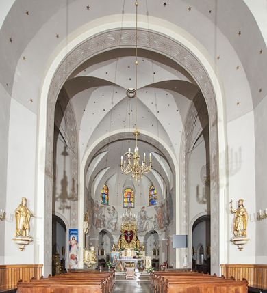 Zdjęcie nr 111: Kościół murowany, orientowany, jednonawowy, z transeptem, prezbiterium z obejściem i przybudówkami. Od zachodu kruchta, od północy kwadratowa kaplica, od południa kolejna przybudówka. 
Prezbiterium zamknięte półokrągło, z obejściem przeprutym do niego arkadami wspartymi na filarach. Ściany nawy i prezbiterium gładkie, przekryte sklepieniem kolebkowym z lunetami, w których mieszczą się okna. Transept i przecięcie naw sklepione krzyżowo. Na ścianach polichromia figuralna ze scenami z Nowego Testamentu, w partii sklepienia drobne, złote gwiazdki. Od zachodu chór zatopiony w występującym asymetrycznie murze, z tralkową balustradą. W prezbiterium siedem okien w kształcie stojącego prostokąta zamkniętego łukiem pełnym wypełnionych witrażami, w nawie sześć okien, w ramionach transeptu po jednym, czterodzielnym, wypełnionym witrażem, na wysokości chóru po dwa z każdej strony. Główne wejście od zachodu przez kruchtę. Fasada poprzedzona przedsionkiem o podziałach ramowych, z prostokątnym wejściem na osi, flankowanym parą pilastrów i prostokątnymi płycinami. Kondygnację wieńczy pełne belkowanie z wysuniętym gzymsem podtrzymującym daszek i trójkątny, schodkowy szczyt zakończony postumentami. Na centralnym krzyż, na sąsiadujących figury dzieci z rogami obfitości, a na zewnętrznych wazony płomieniste; szczyt ujmują postumenty z kulami. Fasada dwukondygnacyjna ze szczytem. Kondygnacja trójosiowa, rozdzielona pilastrami, o polach wypełnionych blendami w kształcie stojących prostokątów zamkniętych łukiem pełnym; szczyt trójkątny, z tarczą zegarową pośrodku. Budynek kościoła o wyraźnych podziałach na bryły składowe, ściany gładkie, przeprute oknami, z gzymsami pod krawędziami dachu. 
Nad nawą główną, na kalenicy, wieżyczka na sygnaturkę z latarnią i baniastym hełmem, druga na skrzyżowaniu naw, z latarnią i  hełmem zakończonym krzyżem. Dach nad nawą główną i przedsionkiem dwuspadowy, nad ramionami transeptu trójspadowym,nad prezbiterium zakończony wielobocznie, na przybudówkach dachy pulpitowe, dwuspadowe i wielospadowe. Dachy kryte dachówką ceramiczną, wieżyczki blachą. 
Najciekawszymi zabytkami kościoła są ołtarz główny z około 1700 roku z nastawą utworzoną z wici winnej latorośli, manierystyczny ołtarz boczny oraz siedemnastowieczna chrzcielnica z warsztatu Santi Gucciego. 
