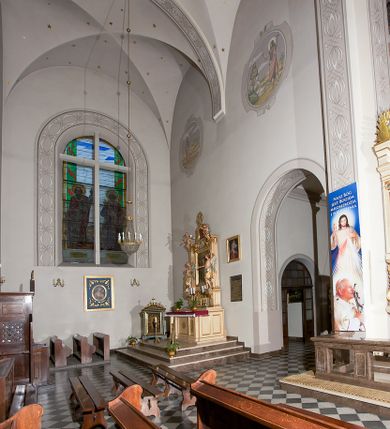 Zdjęcie nr 126: Kościół murowany, orientowany, jednonawowy, z transeptem, prezbiterium z obejściem i przybudówkami. Od zachodu kruchta, od północy kwadratowa kaplica, od południa kolejna przybudówka. 
Prezbiterium zamknięte półokrągło, z obejściem przeprutym do niego arkadami wspartymi na filarach. Ściany nawy i prezbiterium gładkie, przekryte sklepieniem kolebkowym z lunetami, w których mieszczą się okna. Transept i przecięcie naw sklepione krzyżowo. Na ścianach polichromia figuralna ze scenami z Nowego Testamentu, w partii sklepienia drobne, złote gwiazdki. Od zachodu chór zatopiony w występującym asymetrycznie murze, z tralkową balustradą. W prezbiterium siedem okien w kształcie stojącego prostokąta zamkniętego łukiem pełnym wypełnionych witrażami, w nawie sześć okien, w ramionach transeptu po jednym, czterodzielnym, wypełnionym witrażem, na wysokości chóru po dwa z każdej strony. Główne wejście od zachodu przez kruchtę. Fasada poprzedzona przedsionkiem o podziałach ramowych, z prostokątnym wejściem na osi, flankowanym parą pilastrów i prostokątnymi płycinami. Kondygnację wieńczy pełne belkowanie z wysuniętym gzymsem podtrzymującym daszek i trójkątny, schodkowy szczyt zakończony postumentami. Na centralnym krzyż, na sąsiadujących figury dzieci z rogami obfitości, a na zewnętrznych wazony płomieniste; szczyt ujmują postumenty z kulami. Fasada dwukondygnacyjna ze szczytem. Kondygnacja trójosiowa, rozdzielona pilastrami, o polach wypełnionych blendami w kształcie stojących prostokątów zamkniętych łukiem pełnym; szczyt trójkątny, z tarczą zegarową pośrodku. Budynek kościoła o wyraźnych podziałach na bryły składowe, ściany gładkie, przeprute oknami, z gzymsami pod krawędziami dachu. 
Nad nawą główną, na kalenicy, wieżyczka na sygnaturkę z latarnią i baniastym hełmem, druga na skrzyżowaniu naw, z latarnią i  hełmem zakończonym krzyżem. Dach nad nawą główną i przedsionkiem dwuspadowy, nad ramionami transeptu trójspadowym,nad prezbiterium zakończony wielobocznie, na przybudówkach dachy pulpitowe, dwuspadowe i wielospadowe. Dachy kryte dachówką ceramiczną, wieżyczki blachą. 
Najciekawszymi zabytkami kościoła są ołtarz główny z około 1700 roku z nastawą utworzoną z wici winnej latorośli, manierystyczny ołtarz boczny oraz siedemnastowieczna chrzcielnica z warsztatu Santi Gucciego. 
