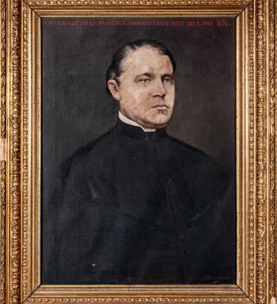 Zdjęcie nr 1: Obraz w formie stojącego prostokąta, w profilowanej ramie zdobionej wiciami roślinnymi. Na ciemnym tle przedstawione w trzech czwartych popiersie księdza ubranego w sutannę i mucet. Twarz o poważnym wyrazie, prostych ustach, szarych  i niewielkich oczach. Na głowie ciemne, siwiejące włosy zaczesane na bok, z wyraźną łysiną. Wzdłuż górnej krawędzi obrazu napis: "CASIMIRUS de OSZACKI. PAROCHUS MORAVICENSIS. OBIIT DIE 8. JUNII 1876 a[nno]" 
W prawym dolnym rogu sygnatura: "T[adeusz] Gadomski 1903."