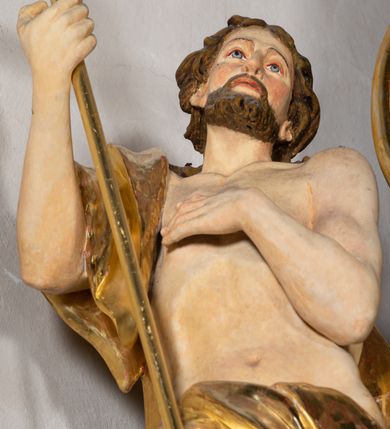 Zdjęcie nr 5: Rzeźba wydrążona z tyłu. Postać Jana Chrzciciela stojąca w kontrapoście z prawą nogą ugiętą, głowa zwrócona w trzech czwartych na lewo. Prawa ręka zgięta w łokciu uniesiona, lewa zgięta z dłonią na piersi. Twarz zakończona ostrym podbródkiem okolonym brodą, rozchylone usta, otwarte oczy, prosty nos, wąskie ciemne brwi, wyraźne rysy z podkreślonymi kośćmi policzkowymi. Na głowie brązowe włosy w postaci loków spływające na plecy. Na prawe ramię zarzucona skóra wielbłąda. Święty w biodrach przepasany tkaniną przewieszoną przez sznur o wyraźnych, obfitych fałdowaniach. Sylwetka z poprawnie i wyraźnie zaznaczoną muskulaturą. Święty trzyma w ręku długi krzyż, a przy nogach leży baranek. Szaty i krzyż złocone, polichromia partii ciała naturalistyczna, figura baranka srebrzona. 