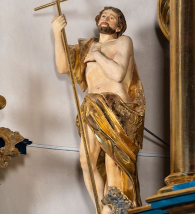 Zdjęcie nr 1: Rzeźba wydrążona z tyłu. Postać Jana Chrzciciela stojąca w kontrapoście z prawą nogą ugiętą, głowa zwrócona w trzech czwartych na lewo. Prawa ręka zgięta w łokciu uniesiona, lewa zgięta z dłonią na piersi. Twarz zakończona ostrym podbródkiem okolonym brodą, rozchylone usta, otwarte oczy, prosty nos, wąskie ciemne brwi, wyraźne rysy z podkreślonymi kośćmi policzkowymi. Na głowie brązowe włosy w postaci loków spływające na plecy. Na prawe ramię zarzucona skóra wielbłąda. Święty w biodrach przepasany tkaniną przewieszoną przez sznur o wyraźnych, obfitych fałdowaniach. Sylwetka z poprawnie i wyraźnie zaznaczoną muskulaturą. Święty trzyma w ręku długi krzyż, a przy nogach leży baranek. Szaty i krzyż złocone, polichromia partii ciała naturalistyczna, figura baranka srebrzona. 