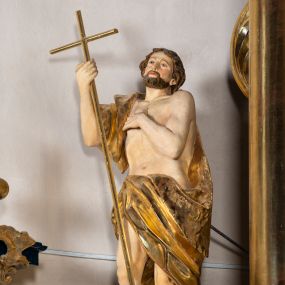 Zdjęcie nr 1: Rzeźba wydrążona z tyłu. Postać Jana Chrzciciela stojąca w kontrapoście z prawą nogą ugiętą, głowa zwrócona w trzech czwartych na lewo. Prawa ręka zgięta w łokciu uniesiona, lewa zgięta z dłonią na piersi. Twarz zakończona ostrym podbródkiem okolonym brodą, rozchylone usta, otwarte oczy, prosty nos, wąskie ciemne brwi, wyraźne rysy z podkreślonymi kośćmi policzkowymi. Na głowie brązowe włosy w postaci loków spływające na plecy. Na prawe ramię zarzucona skóra wielbłąda. Święty w biodrach przepasany tkaniną przewieszoną przez sznur o wyraźnych, obfitych fałdowaniach. Sylwetka z poprawnie i wyraźnie zaznaczoną muskulaturą. Święty trzyma w ręku długi krzyż, a przy nogach leży baranek. Szaty i krzyż złocone, polichromia partii ciała naturalistyczna, figura baranka srebrzona. 