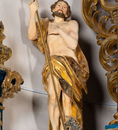 Zdjęcie nr 3: Rzeźba wydrążona z tyłu. Postać Jana Chrzciciela stojąca w kontrapoście z prawą nogą ugiętą, głowa zwrócona w trzech czwartych na lewo. Prawa ręka zgięta w łokciu uniesiona, lewa zgięta z dłonią na piersi. Twarz zakończona ostrym podbródkiem okolonym brodą, rozchylone usta, otwarte oczy, prosty nos, wąskie ciemne brwi, wyraźne rysy z podkreślonymi kośćmi policzkowymi. Na głowie brązowe włosy w postaci loków spływające na plecy. Na prawe ramię zarzucona skóra wielbłąda. Święty w biodrach przepasany tkaniną przewieszoną przez sznur o wyraźnych, obfitych fałdowaniach. Sylwetka z poprawnie i wyraźnie zaznaczoną muskulaturą. Święty trzyma w ręku długi krzyż, a przy nogach leży baranek. Szaty i krzyż złocone, polichromia partii ciała naturalistyczna, figura baranka srebrzona. 