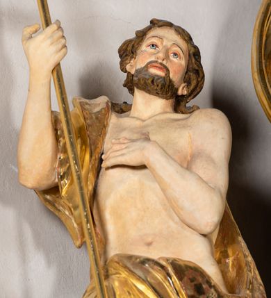 Zdjęcie nr 6: Rzeźba wydrążona z tyłu. Postać Jana Chrzciciela stojąca w kontrapoście z prawą nogą ugiętą, głowa zwrócona w trzech czwartych na lewo. Prawa ręka zgięta w łokciu uniesiona, lewa zgięta z dłonią na piersi. Twarz zakończona ostrym podbródkiem okolonym brodą, rozchylone usta, otwarte oczy, prosty nos, wąskie ciemne brwi, wyraźne rysy z podkreślonymi kośćmi policzkowymi. Na głowie brązowe włosy w postaci loków spływające na plecy. Na prawe ramię zarzucona skóra wielbłąda. Święty w biodrach przepasany tkaniną przewieszoną przez sznur o wyraźnych, obfitych fałdowaniach. Sylwetka z poprawnie i wyraźnie zaznaczoną muskulaturą. Święty trzyma w ręku długi krzyż, a przy nogach leży baranek. Szaty i krzyż złocone, polichromia partii ciała naturalistyczna, figura baranka srebrzona. 