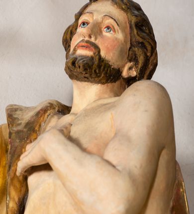 Zdjęcie nr 4: Rzeźba wydrążona, ścięta. Święty Jan Ewangelista ukazany w pozycji stojącej, w swobodnej pozie i znacznym kontrapoście, z lewą nogą ugiętą w kolanie. Jego prawa ręka jest zgięta w łokciu i uniesiona, w lewej przytrzymuje księgę. Głowa zwrócona w trzech czwartych, w prawo. Twarz okolona brodą, z rozchylonymi ustami. Na głowie włosy w postaci loków opadających na plecy. Święty jest ubrany w suknię i płaszcz zebrany w fałdach na lewym boku. Draperie o mocnych fałdowaniach, wyraźne, swobodnie rozwiana tkanina. Szaty i księga złocone, polichromia w partiach ciała naturalistyczna. 