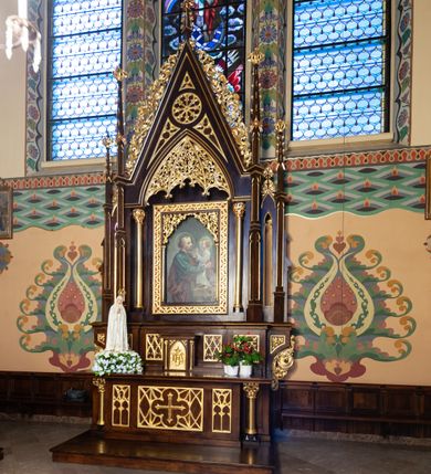 Zdjęcie nr 2: Nastawa ołtarzowa architektoniczna, jednoosiowa, jednokondygnacyjna. Ołtarz prostopadłościenny, drewniany. Antepedium dekorowane trzema płycinami; środkowa w formie leżącego prostokąta z czworoliściem i krzyżem w polu otoczonym siecią ażurowych linii; zewnętrzne w formie stojącego prostokąta z blendami. Mensa drewniana z kamiennym portatylem, podtrzymywana przez parę kolumn o roślinnych kapitelach, flankujących ołtarz. Tabernakulum w formie prostopadłościennej skrzynki; na froncie ryzalit z drzwiczkami w formie stojącego prostokąta zamkniętego łukiem ostrym, w opasce z rzeźbionym i aplikowanym monogramem IHS na groszkowanym tle; w przyłuczach płyciny z rzeźbionymi liśćmi ostrokrzewu. Ryzalit flankowany parą kolumienek o stylizowanych kapitelach, dźwigających profilowany gzyms opasujący tabernakulum z trzech stron. 

Retabulum ustawione na predelli dekorowanej płycinami z maswerkiem. Nastawa flankowana parą smukłych kolumienek wspierających dużą wimpergę oraz dwiema parami ukośnie ustawionych pinakli. Pomiędzy pinaklami wąskie ścianki boczne zdobione wąską, ostrołukową arkadką. W polu głównym w szerokiej ramie umieszczony jest obraz św. Józefa z Dzieciątkiem. W świetle ramy wizerunek ujęty dodatkowo kolumienkami podtrzymującymi ażurową dekorację roślinną wypełniającą naroża na kształt łuku ostrego. Pole wimpergi dekorowane rozetą i płycinami z maswerkiem, w dolnej partii z podwieszonym prześwitem, zdobionym roślinną ażurową dekoracją. Gzyms bo bokach wimpergi zdobiony bujną roślinną dekoracją. Całość zakończona pinaklem z krzyżem. Struktura w odcieniu naturalnego drewna; ornamentyka, kolumny i profile złocone.

