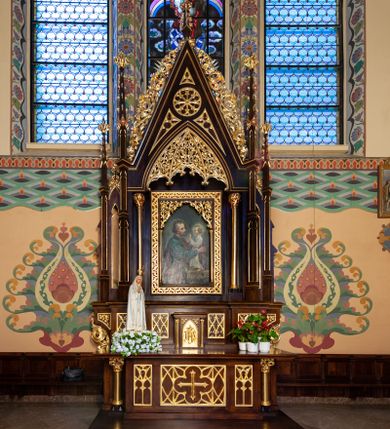 Zdjęcie nr 1: Nastawa ołtarzowa architektoniczna, jednoosiowa, jednokondygnacyjna. Ołtarz prostopadłościenny, drewniany. Antepedium dekorowane trzema płycinami; środkowa w formie leżącego prostokąta z czworoliściem i krzyżem w polu otoczonym siecią ażurowych linii; zewnętrzne w formie stojącego prostokąta z blendami. Mensa drewniana z kamiennym portatylem, podtrzymywana przez parę kolumn o roślinnych kapitelach, flankujących ołtarz. Tabernakulum w formie prostopadłościennej skrzynki; na froncie ryzalit z drzwiczkami w formie stojącego prostokąta zamkniętego łukiem ostrym, w opasce z rzeźbionym i aplikowanym monogramem IHS na groszkowanym tle; w przyłuczach płyciny z rzeźbionymi liśćmi ostrokrzewu. Ryzalit flankowany parą kolumienek o stylizowanych kapitelach, dźwigających profilowany gzyms opasujący tabernakulum z trzech stron. 

Retabulum ustawione na predelli dekorowanej płycinami z maswerkiem. Nastawa flankowana parą smukłych kolumienek wspierających dużą wimpergę oraz dwiema parami ukośnie ustawionych pinakli. Pomiędzy pinaklami wąskie ścianki boczne zdobione wąską, ostrołukową arkadką. W polu głównym w szerokiej ramie umieszczony jest obraz św. Józefa z Dzieciątkiem. W świetle ramy wizerunek ujęty dodatkowo kolumienkami podtrzymującymi ażurową dekorację roślinną wypełniającą naroża na kształt łuku ostrego. Pole wimpergi dekorowane rozetą i płycinami z maswerkiem, w dolnej partii z podwieszonym prześwitem, zdobionym roślinną ażurową dekoracją. Gzyms bo bokach wimpergi zdobiony bujną roślinną dekoracją. Całość zakończona pinaklem z krzyżem. Struktura w odcieniu naturalnego drewna; ornamentyka, kolumny i profile złocone.

