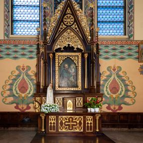 Zdjęcie nr 1: Nastawa ołtarzowa architektoniczna, jednoosiowa, jednokondygnacyjna. Ołtarz prostopadłościenny, drewniany. Antepedium dekorowane trzema płycinami; środkowa w formie leżącego prostokąta z czworoliściem i krzyżem w polu otoczonym siecią ażurowych linii; zewnętrzne w formie stojącego prostokąta z blendami. Mensa drewniana z kamiennym portatylem, podtrzymywana przez parę kolumn o roślinnych kapitelach, flankujących ołtarz. Tabernakulum w formie prostopadłościennej skrzynki; na froncie ryzalit z drzwiczkami w formie stojącego prostokąta zamkniętego łukiem ostrym, w opasce z rzeźbionym i aplikowanym monogramem IHS na groszkowanym tle; w przyłuczach płyciny z rzeźbionymi liśćmi ostrokrzewu. Ryzalit flankowany parą kolumienek o stylizowanych kapitelach, dźwigających profilowany gzyms opasujący tabernakulum z trzech stron. 

Retabulum ustawione na predelli dekorowanej płycinami z maswerkiem. Nastawa flankowana parą smukłych kolumienek wspierających dużą wimpergę oraz dwiema parami ukośnie ustawionych pinakli. Pomiędzy pinaklami wąskie ścianki boczne zdobione wąską, ostrołukową arkadką. W polu głównym w szerokiej ramie umieszczony jest obraz św. Józefa z Dzieciątkiem. W świetle ramy wizerunek ujęty dodatkowo kolumienkami podtrzymującymi ażurową dekorację roślinną wypełniającą naroża na kształt łuku ostrego. Pole wimpergi dekorowane rozetą i płycinami z maswerkiem, w dolnej partii z podwieszonym prześwitem, zdobionym roślinną ażurową dekoracją. Gzyms bo bokach wimpergi zdobiony bujną roślinną dekoracją. Całość zakończona pinaklem z krzyżem. Struktura w odcieniu naturalnego drewna; ornamentyka, kolumny i profile złocone.

