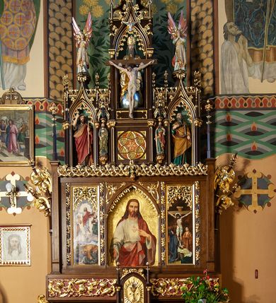 Zdjęcie nr 1: Nastawa ołtarzowa architektoniczna, jednoosiowa, jednokondygnacyjna ze zwieńczeniem, ustawiona na stopniu. Ołtarz prostopadłościenny, drewniany. Antepedium dekorowane trzema płycinami; środkowa w formie wieloliścia z krzyżem w polu, po jej obu stronach złocone płyciny prostokątne zakończone łukiem ostrym z laskowaniem, maswerkiem w zwieńczeniu i wicią roślinną po obu stronach laskowania. Mensa oparta jest na czterech wolno stojących kolumnach z trzonami zdobionymi motywem okręgów z wpisanymi w nie krzyżami greckimi z kapitelami korynckimi. Tabernakulum w formie prostopadłościennej skrzynki, flankowane parą kolumienek na wysokich cokołach podtrzymujących ostrołukową arkadę; na osi kolumn dwa pinakle zwieńczone kwiatonami. Na ściance frontowej drzwiczki ze złoconą płyciną w kształcie stojącego prostokąta, zamkniętego łukiem ostrym z płaskorzeźbionym kielichem z hostią w polu, obwiedzionym promienistą aureolą; po bokach kielicha dwie gwiazdki. Na gzymsie tabernakulum płaskorzeźbiona wić roślinna.

Predella ustawiona na niskim cokoliku zdobionym rozetami, powyżej wklęsły wałek oraz płycina w kształcie leżącego prostokąta z rzeźbioną wicią roślinną na czerwonym tle. Nastawa flankowana parą smukłych filarów wspierających wąskie pinakle z kwiatonami i żabkami. Pole główne w formie tryptyku, poszczególne kwatery oddzielone pionowymi płycinami zdobionymi płaskorzeźbioną laską, owiniętą liśćmi stylizowanego akantu. W polu głównym obraz „Najświętsze Serce Jezusa” umieszczony w prostokątnej wnęce, zamkniętej łukiem ostrym, podtrzymanym półkolumienkami. W nadłuczach stylizowany astwerk. W lewej kwaterze obraz przedstawiający Przemienienie Pańskie. Z kolei w prawej kwaterze obraz „Ukrzyżowanie”. Gzyms kondygnacji ozdobiony jest rzeźbionym astwerkiem. Po bokach kondygnacji dwie pary wygiętych, delikatnie esowato pinakli owiniętych wolutowo zawiniętymi liśćmi stylizowanego akantu.

Zwieńczenie trójosiowe, w kształcie trzech ostrołukowych aediculi wspartych zdwojonymi kolumienkami. Pomiędzy osiami podwieszone baldachimy, pod którymi ustawione są na wspornikach dwie rzeźby: po lewej stronie św. Piotra, a po prawej św. Pawła. Oś środkowa jest znacznie wyższa od bocznych, posadowiona na wysokim cokole, w którym znajduje się maswerk, flankowany pilastrami. Powyżej aedicula z głęboką wnęką, w której umieszczona jest rzeźba przedstawiająca Tron Łaski. Całość zwieńczona dwukondygnacyjnym szczytem z pinaklami, kwiatonami i żabkami. W osi bocznej, lewej w głębokiej wnęce umieszczona jest figura św. Filipa Apostoła, a po prawej stronie zwieńczenia figura św. Andrzeja. Na osi bocznych partii zwieńczenia znajdują się wsporniki z figurami aniołów. Struktura w odcieniu naturalnego drewna; ornamentyka i profile złocone, detale polichromowane.
