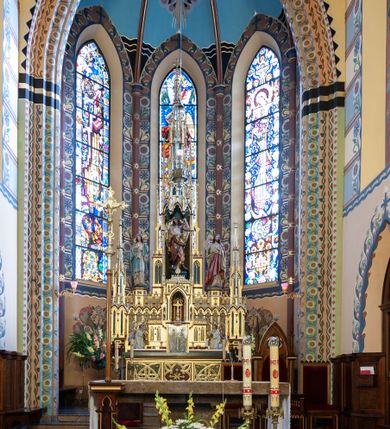 Zdjęcie nr 1: Nastawa ołtarzowa architektoniczna, jednoosiowa, jednokondygnacyjna, ustawiona na cokole. Ołtarz murowany, prostopadłościenny. Mensa betonowa, opasana drewnianymi listwami. Antepedium drewniane w formie leżącego prostokąta, zwieńczone gzymsem; w polu trzy kwadratowe płyciny z maswerkami; ponadto w dwóch zewnętrznych malowana dekoracja roślinna; a w środkowej płaskorzeźbiony, równoramienny krzyż z wiązkami promieni. Na ścianach bocznych ołtarza obudowa drewniana z płycinami. Tabernakulum w formie prostopadłościennej skrzynki, obite złoconą blachą. Drzwiczki dwuskrzydłowe w formie wydłużonego, stojącego prostokąta z aplikowaną dekoracją w postaci odlewanej winnej latorośli. Tron wystawienia trójosiowy. Część środkowa w formie obrotowej niszy o kształcie ostrołuku, flankowany ażurowymi blendami z pinaklami; zwieńczony prostopadłościenną nadstawką, dekorowaną blendami, nakrytą mansardowym, łuskowym zadaszeniem. Nisza dekorowana blendami wydzielonymi przez półkolumienki dźwigające żebra konchy, pola z malowanym winnym gronem. Całość ujmują dwie bryły w formie modeli kościoła; z dwiema parami wysokich, ostrołukowych biforiów oraz dwiema parami szkarp; zamknięte gzymsami z pasem dekoracji maswerkowej, zwieńczone daszkami mansardowymi z łuskami. Tron flankuje para klęczących figur aniołów.

Cokół retabulum wysoki w formie leżącego prostokąta dekorowanego rzędem arkadek w kształcie ostrołukowych blend z malowaną złotem dekoracją roślinną w polach, zwieńczony gzymsem dekorowanym rzeźbionym astwerkiem oraz kwiatonami, zasłaniającymi mansardowy, łuskowy dach cokołu. Część główna nastawy, właściwie umieszczona w partii zwieńczenia. W centrum, ponad tabernakulum wznosi się wieżyczka z głęboką wnęką, w której umieszczona jest figura św. Michała Archanioła. Nisza ujęta jest parą kolumienek wspierających baldachim, nad którym znajduje się kilkukondygnacyjny, ażurowy, dekoracyjny szczyt złożony z pinakli i kwiatonów. Po bokach zwieńczenia umieszczone są dwa ośmioboczne cokoły z figurami: po lewej stronie Matki Boskiej z gorejącym sercem, a po prawej Najświętszego Serca Pana Jezusa. Osie boczne flankowane są dwiemia wieżyczkami o ściankach zdobionych blendami, zamkniętymi pinaklami z żabkami i kwiatonami. Struktura i dekoracja złocone; nisze, blendy i profile polichromowane w kolorze niebieskim i czerwonym.