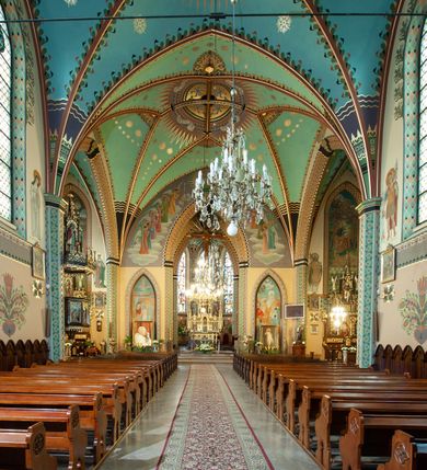 Zdjęcie nr 6: Na dekorację malarską kościoła w Mszanie Dolnej składają się przedstawienia figuralne oraz ornamenty roślinne i fantazyjne. Polichromia ścienna prezbiterium jest bogato dekorowana motywami roślinno-fantazyjnymi. Ościeża okien na ścianie wschodniej zdobią kwiaty chabru, a powyżej na sklepieniu umieszczona jest fantazyjna, promienista gloria z językami ognia, spośród której z szarych obłoków w kształcie płomyków wyłania się Manus Dei. Naroża przęsła malowane są na czarno ze złoconymi falami. Na ścianie północnej prezbiterium w ostrołukowej arkadzie znajduje się przedstawienie Ofiary Melchizedeka, a po przeciwnej stronie Ofiary Abrahama. Całość dopełniają na ościeżach i pozostałych partiach ścian motywy kwiatowe i fantazyjne z przewagą kwiatów chabru i stylizowanych pąków. Tło ścian jest w kolorze beżowym, sklepienie w drugim przęśle prezbiterium malowane jest na niebiesko z analogiczną jak w części wschodniej malowaną promienistą glorią z językami ognia. 

Wschodnia ściana arkady tęczowej podzielona jest na dwie strefy. Dolna część malowana jest na kolor żółty, a w ostrołukowych płycinach umieszczone są dwie sceny: Chrzest Chrystusa po lewej stronie i Kazanie na Górze po prawej stronie. W górnej partii po obu stronach arkady na tle malowanym w kolorze zgaszonego fioletu ukazane są postacie dwunastu aniołów z kwiatami, świecami i kadzielnicami w dłoniach. Na szczycie arkady znajduje się przedstawienie Baranka Bożego, z którego piersi tryska do stojącego obok kielicha krew. Naroża przęsła malowane są na czarno ze złoconymi falami. 

W północnym ramieniu transeptu na ścianie wschodniej umieszczona jest scena Zwiastowania, a po bokach św. Jadwiga Królowa i św. Kinga. Na przeciwnej ścianie znajduje się uskrzydlona główka aniołka podtrzymująca fantazyjny kartusz z napisem: „A SŁOWO / STAŁO SIĘ / CIAŁEM”. W południowym ramieniu transeptu na ścianie wschodniej w ostrołukowej płycinie umieszczone jest przedstawienie św. Józefa z Dzieciątkiem, a po bokach ściany św. Wojciech po lewej stronie i św. Stanisław z Piotrowinem po prawej stronie. Po przeciwnej stronie kaplicy słowa „BĄDŹ WOLA TWOJA” otoczone kwiatami polnego ostu.

Sklepienie na skrzyżowaniu nawy głównej z transeptem pokryte jest złoconymi gwiazdami na niebieskim tle. W centrum umieszczona jest bordowo-niebieska promienista gloria, w środku której na złoconym tle znajują się hierogramy, a na obrzeżach banderole z napisami: „VINCES”, „IN HOC SIGNO”, „VINCES”, „IN HOC SIGNO”. Żebra sklepienie malowane są w pasy w kolorze czerwonym, czarnym i złotym, a na brzegach zdobione fantazyjną, drobną dekoracją.

Nawa główna podzielona jest na dwie strefy. W dolnej na beżowym tle w każdym przęśle nawy znajduje się fantazyjny bukiet kwiatów. Strefy oddzielone są od siebie szerokim pasem w kolorze zgaszonego fioletu, ozdobionego rzędem naprzemiennie białych i żółtych czteropłatkowych kwiatów na ulistnionych gałązkach. W górnej strefie na beżowym tle umieszczone są postacie świętych opatrzone podpisami. Na ścianie północnej od zachodu: „ŚW(IĘTA BARBARA”, „BŁ(OGOSŁAWIONA) SALOMEA”, „ŚW(IĘTA) KATARZYNA” i „BŁ(OGOSŁAWIONA) BRONISŁAWA”. Na ścianie południowej od zachodu: ŚW(IĘTY) ST(ANISŁAW) KOSTKA”, „ŚW(IĘTY) JAN KANTY”, „ŚW(IĘTY) KAZIMIERZ” i „ŚW(IĘTY) FLORIAN”. Ościeża okien w nawie głównej zdobi geometryczna siatka w kolorze zielono-pomarańczowym, a dookoła kwiaty łubinu i bazie. Z kolei przyścienne kolumny, ostrołukowe profilowane przejścia transeptu i nawy głównej zdobią słoneczniki, trójlistne koniczyny oraz pawie oczka.  Dekoracja ornamentalna sklepień w nawie głównej jest podobna, jak w poprzednio opisanych częściach świątyni. 

Na chórze znajduje się przedstawienia św. Franciszka z Asyżu po lewej stronie i św. Cecylii po prawej, a pośrodku słowa „UWIELBIAJ DUSZO MOJA PANA” w fantazyjnej glorii. 
