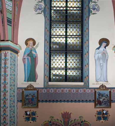 Zdjęcie nr 12: Na dekorację malarską kościoła w Mszanie Dolnej składają się przedstawienia figuralne oraz ornamenty roślinne i fantazyjne. Polichromia ścienna prezbiterium jest bogato dekorowana motywami roślinno-fantazyjnymi. Ościeża okien na ścianie wschodniej zdobią kwiaty chabru, a powyżej na sklepieniu umieszczona jest fantazyjna, promienista gloria z językami ognia, spośród której z szarych obłoków w kształcie płomyków wyłania się Manus Dei. Naroża przęsła malowane są na czarno ze złoconymi falami. Na ścianie północnej prezbiterium w ostrołukowej arkadzie znajduje się przedstawienie Ofiary Melchizedeka, a po przeciwnej stronie Ofiary Abrahama. Całość dopełniają na ościeżach i pozostałych partiach ścian motywy kwiatowe i fantazyjne z przewagą kwiatów chabru i stylizowanych pąków. Tło ścian jest w kolorze beżowym, sklepienie w drugim przęśle prezbiterium malowane jest na niebiesko z analogiczną jak w części wschodniej malowaną promienistą glorią z językami ognia. 

Wschodnia ściana arkady tęczowej podzielona jest na dwie strefy. Dolna część malowana jest na kolor żółty, a w ostrołukowych płycinach umieszczone są dwie sceny: Chrzest Chrystusa po lewej stronie i Kazanie na Górze po prawej stronie. W górnej partii po obu stronach arkady na tle malowanym w kolorze zgaszonego fioletu ukazane są postacie dwunastu aniołów z kwiatami, świecami i kadzielnicami w dłoniach. Na szczycie arkady znajduje się przedstawienie Baranka Bożego, z którego piersi tryska do stojącego obok kielicha krew. Naroża przęsła malowane są na czarno ze złoconymi falami. 

W północnym ramieniu transeptu na ścianie wschodniej umieszczona jest scena Zwiastowania, a po bokach św. Jadwiga Królowa i św. Kinga. Na przeciwnej ścianie znajduje się uskrzydlona główka aniołka podtrzymująca fantazyjny kartusz z napisem: „A SŁOWO / STAŁO SIĘ / CIAŁEM”. W południowym ramieniu transeptu na ścianie wschodniej w ostrołukowej płycinie umieszczone jest przedstawienie św. Józefa z Dzieciątkiem, a po bokach ściany św. Wojciech po lewej stronie i św. Stanisław z Piotrowinem po prawej stronie. Po przeciwnej stronie kaplicy słowa „BĄDŹ WOLA TWOJA” otoczone kwiatami polnego ostu.

Sklepienie na skrzyżowaniu nawy głównej z transeptem pokryte jest złoconymi gwiazdami na niebieskim tle. W centrum umieszczona jest bordowo-niebieska promienista gloria, w środku której na złoconym tle znajują się hierogramy, a na obrzeżach banderole z napisami: „VINCES”, „IN HOC SIGNO”, „VINCES”, „IN HOC SIGNO”. Żebra sklepienie malowane są w pasy w kolorze czerwonym, czarnym i złotym, a na brzegach zdobione fantazyjną, drobną dekoracją.

Nawa główna podzielona jest na dwie strefy. W dolnej na beżowym tle w każdym przęśle nawy znajduje się fantazyjny bukiet kwiatów. Strefy oddzielone są od siebie szerokim pasem w kolorze zgaszonego fioletu, ozdobionego rzędem naprzemiennie białych i żółtych czteropłatkowych kwiatów na ulistnionych gałązkach. W górnej strefie na beżowym tle umieszczone są postacie świętych opatrzone podpisami. Na ścianie północnej od zachodu: „ŚW(IĘTA BARBARA”, „BŁ(OGOSŁAWIONA) SALOMEA”, „ŚW(IĘTA) KATARZYNA” i „BŁ(OGOSŁAWIONA) BRONISŁAWA”. Na ścianie południowej od zachodu: ŚW(IĘTY) ST(ANISŁAW) KOSTKA”, „ŚW(IĘTY) JAN KANTY”, „ŚW(IĘTY) KAZIMIERZ” i „ŚW(IĘTY) FLORIAN”. Ościeża okien w nawie głównej zdobi geometryczna siatka w kolorze zielono-pomarańczowym, a dookoła kwiaty łubinu i bazie. Z kolei przyścienne kolumny, ostrołukowe profilowane przejścia transeptu i nawy głównej zdobią słoneczniki, trójlistne koniczyny oraz pawie oczka.  Dekoracja ornamentalna sklepień w nawie głównej jest podobna, jak w poprzednio opisanych częściach świątyni. 

Na chórze znajduje się przedstawienia św. Franciszka z Asyżu po lewej stronie i św. Cecylii po prawej, a pośrodku słowa „UWIELBIAJ DUSZO MOJA PANA” w fantazyjnej glorii. 
