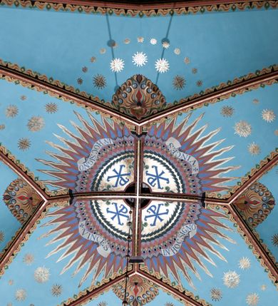 Zdjęcie nr 1: Na dekorację malarską kościoła w Mszanie Dolnej składają się przedstawienia figuralne oraz ornamenty roślinne i fantazyjne. Polichromia ścienna prezbiterium jest bogato dekorowana motywami roślinno-fantazyjnymi. Ościeża okien na ścianie wschodniej zdobią kwiaty chabru, a powyżej na sklepieniu umieszczona jest fantazyjna, promienista gloria z językami ognia, spośród której z szarych obłoków w kształcie płomyków wyłania się Manus Dei. Naroża przęsła malowane są na czarno ze złoconymi falami. Na ścianie północnej prezbiterium w ostrołukowej arkadzie znajduje się przedstawienie Ofiary Melchizedeka, a po przeciwnej stronie Ofiary Abrahama. Całość dopełniają na ościeżach i pozostałych partiach ścian motywy kwiatowe i fantazyjne z przewagą kwiatów chabru i stylizowanych pąków. Tło ścian jest w kolorze beżowym, sklepienie w drugim przęśle prezbiterium malowane jest na niebiesko z analogiczną jak w części wschodniej malowaną promienistą glorią z językami ognia. 

Wschodnia ściana arkady tęczowej podzielona jest na dwie strefy. Dolna część malowana jest na kolor żółty, a w ostrołukowych płycinach umieszczone są dwie sceny: Chrzest Chrystusa po lewej stronie i Kazanie na Górze po prawej stronie. W górnej partii po obu stronach arkady na tle malowanym w kolorze zgaszonego fioletu ukazane są postacie dwunastu aniołów z kwiatami, świecami i kadzielnicami w dłoniach. Na szczycie arkady znajduje się przedstawienie Baranka Bożego, z którego piersi tryska do stojącego obok kielicha krew. Naroża przęsła malowane są na czarno ze złoconymi falami. 

W północnym ramieniu transeptu na ścianie wschodniej umieszczona jest scena Zwiastowania, a po bokach św. Jadwiga Królowa i św. Kinga. Na przeciwnej ścianie znajduje się uskrzydlona główka aniołka podtrzymująca fantazyjny kartusz z napisem: „A SŁOWO / STAŁO SIĘ / CIAŁEM”. W południowym ramieniu transeptu na ścianie wschodniej w ostrołukowej płycinie umieszczone jest przedstawienie św. Józefa z Dzieciątkiem, a po bokach ściany św. Wojciech po lewej stronie i św. Stanisław z Piotrowinem po prawej stronie. Po przeciwnej stronie kaplicy słowa „BĄDŹ WOLA TWOJA” otoczone kwiatami polnego ostu.

Sklepienie na skrzyżowaniu nawy głównej z transeptem pokryte jest złoconymi gwiazdami na niebieskim tle. W centrum umieszczona jest bordowo-niebieska promienista gloria, w środku której na złoconym tle znajują się hierogramy, a na obrzeżach banderole z napisami: „VINCES”, „IN HOC SIGNO”, „VINCES”, „IN HOC SIGNO”. Żebra sklepienie malowane są w pasy w kolorze czerwonym, czarnym i złotym, a na brzegach zdobione fantazyjną, drobną dekoracją.

Nawa główna podzielona jest na dwie strefy. W dolnej na beżowym tle w każdym przęśle nawy znajduje się fantazyjny bukiet kwiatów. Strefy oddzielone są od siebie szerokim pasem w kolorze zgaszonego fioletu, ozdobionego rzędem naprzemiennie białych i żółtych czteropłatkowych kwiatów na ulistnionych gałązkach. W górnej strefie na beżowym tle umieszczone są postacie świętych opatrzone podpisami. Na ścianie północnej od zachodu: „ŚW(IĘTA BARBARA”, „BŁ(OGOSŁAWIONA) SALOMEA”, „ŚW(IĘTA) KATARZYNA” i „BŁ(OGOSŁAWIONA) BRONISŁAWA”. Na ścianie południowej od zachodu: ŚW(IĘTY) ST(ANISŁAW) KOSTKA”, „ŚW(IĘTY) JAN KANTY”, „ŚW(IĘTY) KAZIMIERZ” i „ŚW(IĘTY) FLORIAN”. Ościeża okien w nawie głównej zdobi geometryczna siatka w kolorze zielono-pomarańczowym, a dookoła kwiaty łubinu i bazie. Z kolei przyścienne kolumny, ostrołukowe profilowane przejścia transeptu i nawy głównej zdobią słoneczniki, trójlistne koniczyny oraz pawie oczka.  Dekoracja ornamentalna sklepień w nawie głównej jest podobna, jak w poprzednio opisanych częściach świątyni. 

Na chórze znajduje się przedstawienia św. Franciszka z Asyżu po lewej stronie i św. Cecylii po prawej, a pośrodku słowa „UWIELBIAJ DUSZO MOJA PANA” w fantazyjnej glorii. 
