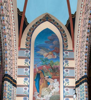 Zdjęcie nr 10: Na dekorację malarską kościoła w Mszanie Dolnej składają się przedstawienia figuralne oraz ornamenty roślinne i fantazyjne. Polichromia ścienna prezbiterium jest bogato dekorowana motywami roślinno-fantazyjnymi. Ościeża okien na ścianie wschodniej zdobią kwiaty chabru, a powyżej na sklepieniu umieszczona jest fantazyjna, promienista gloria z językami ognia, spośród której z szarych obłoków w kształcie płomyków wyłania się Manus Dei. Naroża przęsła malowane są na czarno ze złoconymi falami. Na ścianie północnej prezbiterium w ostrołukowej arkadzie znajduje się przedstawienie Ofiary Melchizedeka, a po przeciwnej stronie Ofiary Abrahama. Całość dopełniają na ościeżach i pozostałych partiach ścian motywy kwiatowe i fantazyjne z przewagą kwiatów chabru i stylizowanych pąków. Tło ścian jest w kolorze beżowym, sklepienie w drugim przęśle prezbiterium malowane jest na niebiesko z analogiczną jak w części wschodniej malowaną promienistą glorią z językami ognia. 

Wschodnia ściana arkady tęczowej podzielona jest na dwie strefy. Dolna część malowana jest na kolor żółty, a w ostrołukowych płycinach umieszczone są dwie sceny: Chrzest Chrystusa po lewej stronie i Kazanie na Górze po prawej stronie. W górnej partii po obu stronach arkady na tle malowanym w kolorze zgaszonego fioletu ukazane są postacie dwunastu aniołów z kwiatami, świecami i kadzielnicami w dłoniach. Na szczycie arkady znajduje się przedstawienie Baranka Bożego, z którego piersi tryska do stojącego obok kielicha krew. Naroża przęsła malowane są na czarno ze złoconymi falami. 

W północnym ramieniu transeptu na ścianie wschodniej umieszczona jest scena Zwiastowania, a po bokach św. Jadwiga Królowa i św. Kinga. Na przeciwnej ścianie znajduje się uskrzydlona główka aniołka podtrzymująca fantazyjny kartusz z napisem: „A SŁOWO / STAŁO SIĘ / CIAŁEM”. W południowym ramieniu transeptu na ścianie wschodniej w ostrołukowej płycinie umieszczone jest przedstawienie św. Józefa z Dzieciątkiem, a po bokach ściany św. Wojciech po lewej stronie i św. Stanisław z Piotrowinem po prawej stronie. Po przeciwnej stronie kaplicy słowa „BĄDŹ WOLA TWOJA” otoczone kwiatami polnego ostu.

Sklepienie na skrzyżowaniu nawy głównej z transeptem pokryte jest złoconymi gwiazdami na niebieskim tle. W centrum umieszczona jest bordowo-niebieska promienista gloria, w środku której na złoconym tle znajują się hierogramy, a na obrzeżach banderole z napisami: „VINCES”, „IN HOC SIGNO”, „VINCES”, „IN HOC SIGNO”. Żebra sklepienie malowane są w pasy w kolorze czerwonym, czarnym i złotym, a na brzegach zdobione fantazyjną, drobną dekoracją.

Nawa główna podzielona jest na dwie strefy. W dolnej na beżowym tle w każdym przęśle nawy znajduje się fantazyjny bukiet kwiatów. Strefy oddzielone są od siebie szerokim pasem w kolorze zgaszonego fioletu, ozdobionego rzędem naprzemiennie białych i żółtych czteropłatkowych kwiatów na ulistnionych gałązkach. W górnej strefie na beżowym tle umieszczone są postacie świętych opatrzone podpisami. Na ścianie północnej od zachodu: „ŚW(IĘTA BARBARA”, „BŁ(OGOSŁAWIONA) SALOMEA”, „ŚW(IĘTA) KATARZYNA” i „BŁ(OGOSŁAWIONA) BRONISŁAWA”. Na ścianie południowej od zachodu: ŚW(IĘTY) ST(ANISŁAW) KOSTKA”, „ŚW(IĘTY) JAN KANTY”, „ŚW(IĘTY) KAZIMIERZ” i „ŚW(IĘTY) FLORIAN”. Ościeża okien w nawie głównej zdobi geometryczna siatka w kolorze zielono-pomarańczowym, a dookoła kwiaty łubinu i bazie. Z kolei przyścienne kolumny, ostrołukowe profilowane przejścia transeptu i nawy głównej zdobią słoneczniki, trójlistne koniczyny oraz pawie oczka.  Dekoracja ornamentalna sklepień w nawie głównej jest podobna, jak w poprzednio opisanych częściach świątyni. 

Na chórze znajduje się przedstawienia św. Franciszka z Asyżu po lewej stronie i św. Cecylii po prawej, a pośrodku słowa „UWIELBIAJ DUSZO MOJA PANA” w fantazyjnej glorii. 
