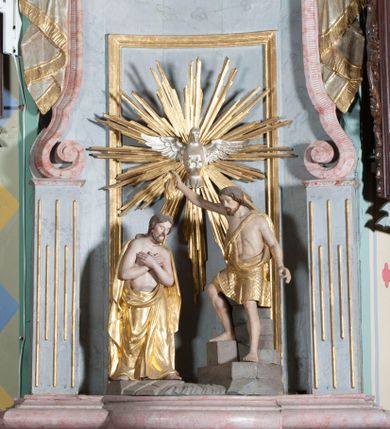 Zdjęcie nr 6: Antyambona złączona z chrzcielnicą. Stopa chrzcielnicy na planie kwadratu, profilowana. Trzon czteroboczny, zwężający się ku górze, w narożach od frontu ujęty listwami. Czara w formie odwróconego, ściętego stożka, z wywiniętą krawędzią. Od spodu opięta pierścieniem i silnie uproszczonym, stylizowanym, żłobkowanym lambrekinem. Pokrywa w formie profilowanego, ściętego stożka, zwieńczonego akantem i szyszką. We wnętrzu czary miedziana misa oraz fragment drewnianej pokrywy z rozetą. Antyambona przyścienna, o wklęsłym licu, na cokole, ujęta filarami podtrzymującymi profilowany gzyms, dekorowanymi płycinami. Pośrodku wspornik w formie wybrzuszonego stożka, o ściętym wierzchołku z grupą rzeźbiarską Chrzest Chrystusa. Powyżej zaplecek ujęty pilastrami, dźwigającymi spływ wolutowe; po bokach udrapowana tkanina. W polu środkowym płycina z rzeźbioną gołębicą Ducha Świętego na tle glorii promienistej. Baldachim na planie odcinka koła, z wyłamującym się gzymsem, dekorowany podwieszonym lambrekinem, zwężający się ku górze, zakończony rokokowym wazonem płomienistym. Struktura marmoryzowana w kolorze jasnoniebieskim, cokół, gzyms i profile jasnoróżowe, dekoracja złocona i srebrzona.