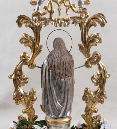 Zdjęcie nr 3: Feretron na profilowanej, prostopadłościennej podstawie z przedstawieniem Maki Boskiej Niepokalanej. Rzeźba pełna została ustawiona na profilowanym cokole, półksiężycu i globie, otoczonym przez wijącego się węża z owocem (jabłkiem) w paszczy. Maria została ukazana frontalnie, w kontrapoście, z dłońmi złożonymi w geście modlitwy, z głową przechyloną na lewe ramię. Twarz ma owalną, o pełnych policzkach i głęboko osadzonych oczach; włosy jasne, długie, opadające na plecy i ramiona. Maria jest ubrana w złotą suknię, o wąskich rękawach i narzucony na ramiona srebrny płaszcz. Figura została ujęta rzeźbionymi liśćmi akantu podtrzymującymi monogram „MARYA” w otoczeniu obłoków i glorii. Polichromia naturalistyczna w odsłoniętych partiach ciała; szaty i dekoracja ornamentalna złocona i srebrzona.