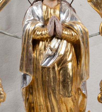 Zdjęcie nr 1: Feretron na profilowanej, prostopadłościennej podstawie z przedstawieniem Maki Boskiej Niepokalanej. Rzeźba pełna została ustawiona na profilowanym cokole, półksiężycu i globie, otoczonym przez wijącego się węża z owocem (jabłkiem) w paszczy. Maria została ukazana frontalnie, w kontrapoście, z dłońmi złożonymi w geście modlitwy, z głową przechyloną na lewe ramię. Twarz ma owalną, o pełnych policzkach i głęboko osadzonych oczach; włosy jasne, długie, opadające na plecy i ramiona. Maria jest ubrana w złotą suknię, o wąskich rękawach i narzucony na ramiona srebrny płaszcz. Figura została ujęta rzeźbionymi liśćmi akantu podtrzymującymi monogram „MARYA” w otoczeniu obłoków i glorii. Polichromia naturalistyczna w odsłoniętych partiach ciała; szaty i dekoracja ornamentalna złocona i srebrzona.