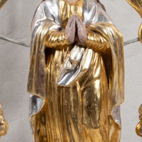 Zdjęcie nr 1: Feretron na profilowanej, prostopadłościennej podstawie z przedstawieniem Maki Boskiej Niepokalanej. Rzeźba pełna została ustawiona na profilowanym cokole, półksiężycu i globie, otoczonym przez wijącego się węża z owocem (jabłkiem) w paszczy. Maria została ukazana frontalnie, w kontrapoście, z dłońmi złożonymi w geście modlitwy, z głową przechyloną na lewe ramię. Twarz ma owalną, o pełnych policzkach i głęboko osadzonych oczach; włosy jasne, długie, opadające na plecy i ramiona. Maria jest ubrana w złotą suknię, o wąskich rękawach i narzucony na ramiona srebrny płaszcz. Figura została ujęta rzeźbionymi liśćmi akantu podtrzymującymi monogram „MARYA” w otoczeniu obłoków i glorii. Polichromia naturalistyczna w odsłoniętych partiach ciała; szaty i dekoracja ornamentalna złocona i srebrzona.