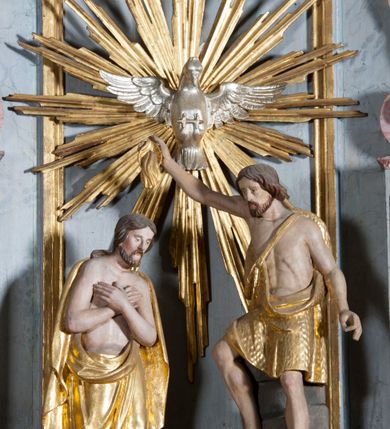 Zdjęcie nr 6: Grupa rzeźbiarska przedstawiająca scenę Chrztu Chrystusa. Rzeźby pełne, całopostaciowe. Po prawej stronie, na blikach skalnych św. Jan Chrzciciel zwrócony w prawo, z prawą nogą ustawioną wyżej, z uniesioną prawą ręką, w której trzyma muszlę z wodą, którą wylewa nad głową Chrystusa. Twarz ma pociągłą, szczupłą, okoloną krótką brodą, włosy półdługie, opadające na kark. Ubrany w osłaniający biodra płaszcz ze skóry, podtrzymywany przez taśmę przewiązaną przez lewe ramię. Po przeciwnej stronie figura Chrystusa zwróconego w trzech czwartych w lewo, w kontrapoście, delikatnie pochylonego z dłońmi skrzyżowanymi na piersi. Twarz pociągła, okolona krótką brodą, włosy długie, opadające na plecy. Na ramiona ma zarzucony płaszcz, biodra przepasane drapowaną tkaniną sięgającą kostek, tors nagi. W tle dużej wielkości gołębica Ducha Świętego na tle glorii promienistej. W odsłoniętych partiach ciała polichromia naturalistyczna, szaty złocone. 