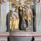 Zdjęcie nr 1: Grupa rzeźbiarska przedstawiająca scenę Chrztu Chrystusa. Rzeźby pełne, całopostaciowe. Po prawej stronie, na blikach skalnych św. Jan Chrzciciel zwrócony w prawo, z prawą nogą ustawioną wyżej, z uniesioną prawą ręką, w której trzyma muszlę z wodą, którą wylewa nad głową Chrystusa. Twarz ma pociągłą, szczupłą, okoloną krótką brodą, włosy półdługie, opadające na kark. Ubrany w osłaniający biodra płaszcz ze skóry, podtrzymywany przez taśmę przewiązaną przez lewe ramię. Po przeciwnej stronie figura Chrystusa zwróconego w trzech czwartych w lewo, w kontrapoście, delikatnie pochylonego z dłońmi skrzyżowanymi na piersi. Twarz pociągła, okolona krótką brodą, włosy długie, opadające na plecy. Na ramiona ma zarzucony płaszcz, biodra przepasane drapowaną tkaniną sięgającą kostek, tors nagi. W tle dużej wielkości gołębica Ducha Świętego na tle glorii promienistej. W odsłoniętych partiach ciała polichromia naturalistyczna, szaty złocone. 