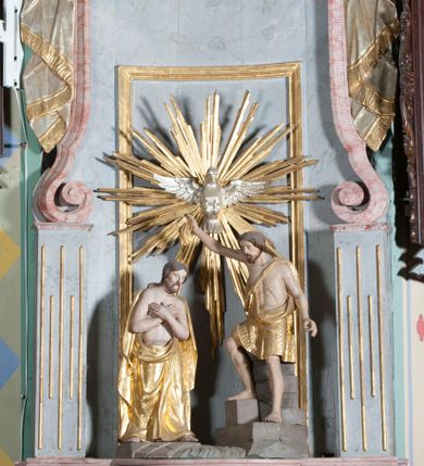 Zdjęcie nr 1: Grupa rzeźbiarska przedstawiająca scenę Chrztu Chrystusa. Rzeźby pełne, całopostaciowe. Po prawej stronie, na blikach skalnych św. Jan Chrzciciel zwrócony w prawo, z prawą nogą ustawioną wyżej, z uniesioną prawą ręką, w której trzyma muszlę z wodą, którą wylewa nad głową Chrystusa. Twarz ma pociągłą, szczupłą, okoloną krótką brodą, włosy półdługie, opadające na kark. Ubrany w osłaniający biodra płaszcz ze skóry, podtrzymywany przez taśmę przewiązaną przez lewe ramię. Po przeciwnej stronie figura Chrystusa zwróconego w trzech czwartych w lewo, w kontrapoście, delikatnie pochylonego z dłońmi skrzyżowanymi na piersi. Twarz pociągła, okolona krótką brodą, włosy długie, opadające na plecy. Na ramiona ma zarzucony płaszcz, biodra przepasane drapowaną tkaniną sięgającą kostek, tors nagi. W tle dużej wielkości gołębica Ducha Świętego na tle glorii promienistej. W odsłoniętych partiach ciała polichromia naturalistyczna, szaty złocone. 