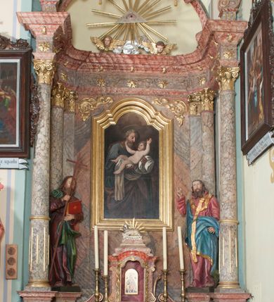 Zdjęcie nr 1: Nastawa ołtarzowa wklęsła, przyjmująca kształt wnęki; jednoosiowa, jednokondygnacyjna ze zwieńczeniem, na podwójnym cokole. Mensa sarkofagowa, wklęsło-wypukła, zwężająca się ku dołowi, ustawiona na dwóch stopniach. Drewniana z marmurowym portatylem z napisem na odwrocie „Anno Domini MDCCCXCIX Die 1. Augusti / Celsissimus ac Reverendissimus Dominus / JOANNES KNIAŹ DE KOZIELSKO / PUZYNA / Princeps Episcopus Cracoviensis altare hoc portatile / consecravit Reliquiasque SS. Cordulae et Rogatae Mill inclusit / Th. Bukowski / Vice custos […]”. Na mensie ustawiono tron wystawienia w formie sześcianu o wypukłej ścianie frontowej, ujęty pilastrami o trzonach w formie wolut, posadowionymi na cokołach. Podpory dźwigają gzyms, wyłamany pośrodku na kształt łuku odcinkowego. Wnęka obrotowa, ujęta ramą w formie wałka, flankowana płaskorzeźbionymi kłosami zbóż; we wnęce ikona Matki Boskiej Nieustającej Pomocy. Całość zwieńczona profilowanym cokołem z przedstawieniem rzeźbionego, leżącego na księdze z pieczęciami Baranka Eucharystycznego w glorii. Pierwsza kondygnacja nastawy ujęta jest ukazanymi na tle pilastrów dwiema parami kompozytowych kolumn, ustawionych w jednej linii; wewnętrzna para pod kątem. Podpory dźwigają pełne belkowanie, delikatnie wyłamane na ich osiach. W polu środkowym obraz z przedstawieniem św. Józefa, w profilowanej ramie w formie stojącego prostokąta; flankowany przez ustawione na niewielkich konsolkach figury św. Cyryla i św. Metodego. Na gzymsie płaskorzeźbione Oko Opatrzności w glorii promienistej, z obłokiem i parą uskrzydlonych główek anielskich. Zwieńczenie w formie czterech kabłąków podtrzymujących diadem zdobiony lambrekinem, ze spływającą po bokach draperią; powyżej cztery kabłąki z gorejącym sercem pośrodku. Cokoły zdobione płycinami z motywem rozet; w jednej trzeciej wysokości trzonów kolumn pierścienie. W przyłuczach ornament roślinny. Fryz zdobiony rozetami. Struktura marmoryzowana, w odcieniach jasnego różu i szarości; ornamentyka i detale złocone i srebrzone.