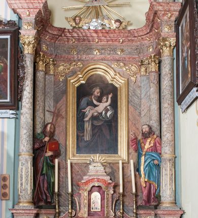 Zdjęcie nr 2: Nastawa ołtarzowa wklęsła, przyjmująca kształt wnęki; jednoosiowa, jednokondygnacyjna ze zwieńczeniem, na podwójnym cokole. Mensa sarkofagowa, wklęsło-wypukła, zwężająca się ku dołowi, ustawiona na dwóch stopniach. Drewniana z marmurowym portatylem z napisem na odwrocie „Anno Domini MDCCCXCIX Die 1. Augusti / Celsissimus ac Reverendissimus Dominus / JOANNES KNIAŹ DE KOZIELSKO / PUZYNA / Princeps Episcopus Cracoviensis altare hoc portatile / consecravit Reliquiasque SS. Cordulae et Rogatae Mill inclusit / Th. Bukowski / Vice custos […]”. Na mensie ustawiono tron wystawienia w formie sześcianu o wypukłej ścianie frontowej, ujęty pilastrami o trzonach w formie wolut, posadowionymi na cokołach. Podpory dźwigają gzyms, wyłamany pośrodku na kształt łuku odcinkowego. Wnęka obrotowa, ujęta ramą w formie wałka, flankowana płaskorzeźbionymi kłosami zbóż; we wnęce ikona Matki Boskiej Nieustającej Pomocy. Całość zwieńczona profilowanym cokołem z przedstawieniem rzeźbionego, leżącego na księdze z pieczęciami Baranka Eucharystycznego w glorii. Pierwsza kondygnacja nastawy ujęta jest ukazanymi na tle pilastrów dwiema parami kompozytowych kolumn, ustawionych w jednej linii; wewnętrzna para pod kątem. Podpory dźwigają pełne belkowanie, delikatnie wyłamane na ich osiach. W polu środkowym obraz z przedstawieniem św. Józefa, w profilowanej ramie w formie stojącego prostokąta; flankowany przez ustawione na niewielkich konsolkach figury św. Cyryla i św. Metodego. Na gzymsie płaskorzeźbione Oko Opatrzności w glorii promienistej, z obłokiem i parą uskrzydlonych główek anielskich. Zwieńczenie w formie czterech kabłąków podtrzymujących diadem zdobiony lambrekinem, ze spływającą po bokach draperią; powyżej cztery kabłąki z gorejącym sercem pośrodku. Cokoły zdobione płycinami z motywem rozet; w jednej trzeciej wysokości trzonów kolumn pierścienie. W przyłuczach ornament roślinny. Fryz zdobiony rozetami. Struktura marmoryzowana, w odcieniach jasnego różu i szarości; ornamentyka i detale złocone i srebrzone.